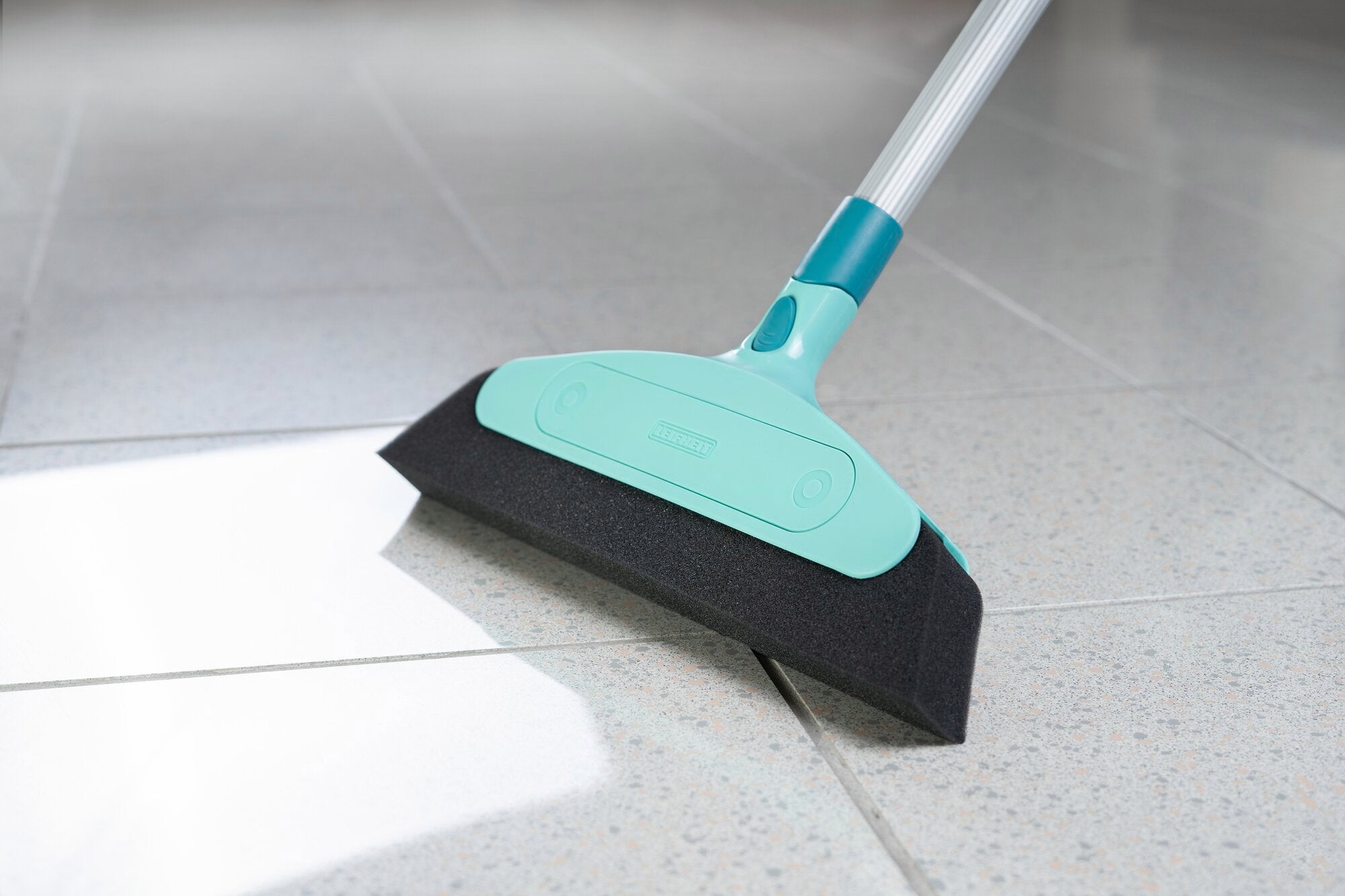 Foam broom with click system on a tiled floor. The broom has a turquoise handle and a black foam edge, ideal for smooth surfaces.