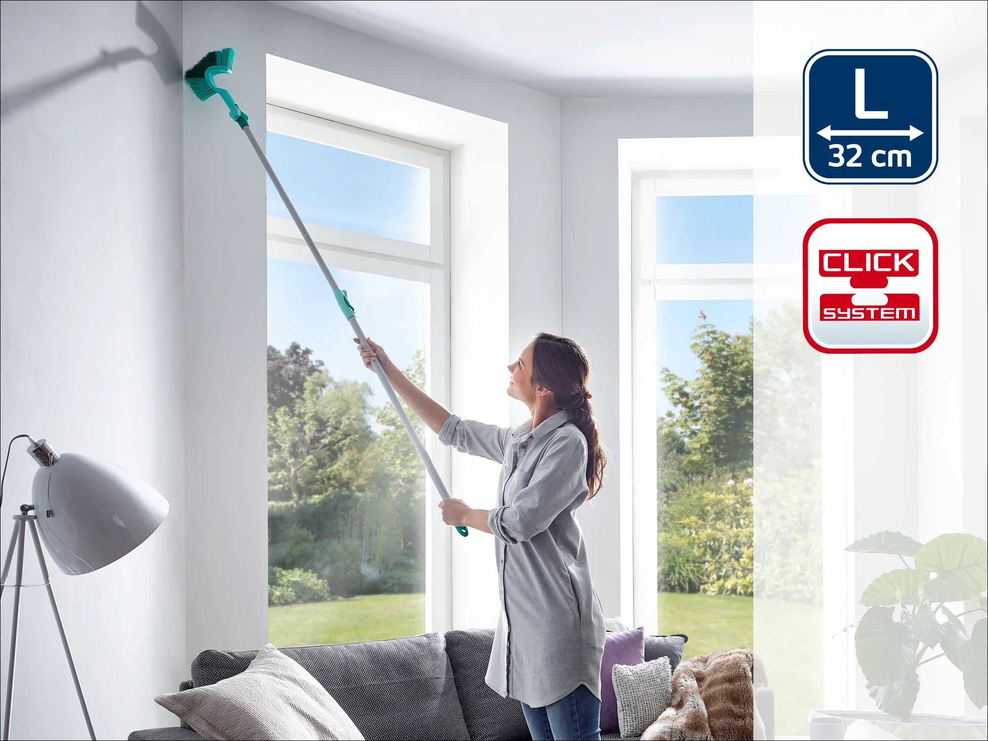 Una mujer limpia una pared alta con un limpiacristales Leifheit Click-System. El limpiacristales tiene una longitud de 32 cm y es ideal para lugares de difícil acceso.