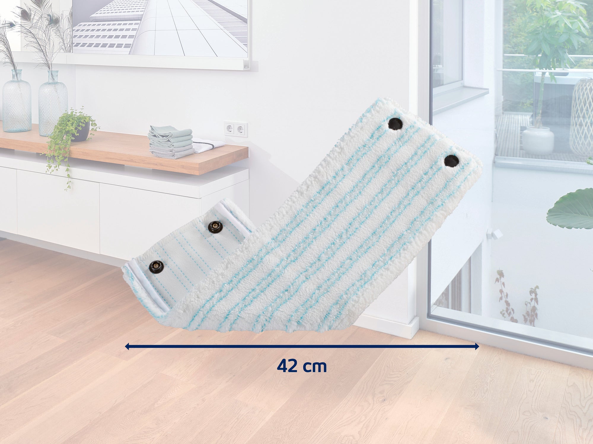 Ein Wischmopp-Aufsatz mit einer Breite von 42 cm liegt in einem modernen, hellen Raum mit Holzboden. Im Hintergrund sind ein Sideboard mit Dekorationen und ein großes Fenster zu sehen.