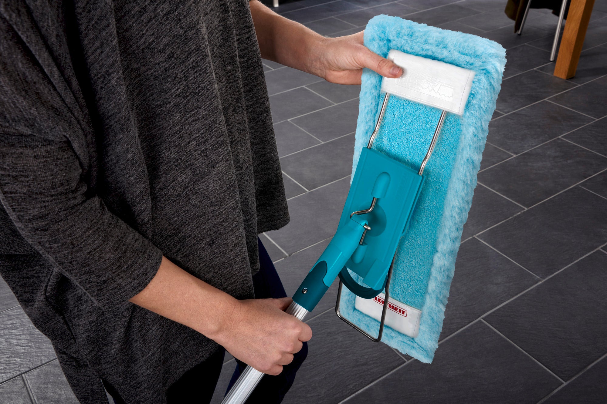 Eén persoon houdt een Profi XL mopovertrek vast. De overtrek heeft een turquoise kleur en wordt gebruikt op een donkere tegelvloer. Ideaal voor grondig schoonmaken en eenvoudig gebruik.