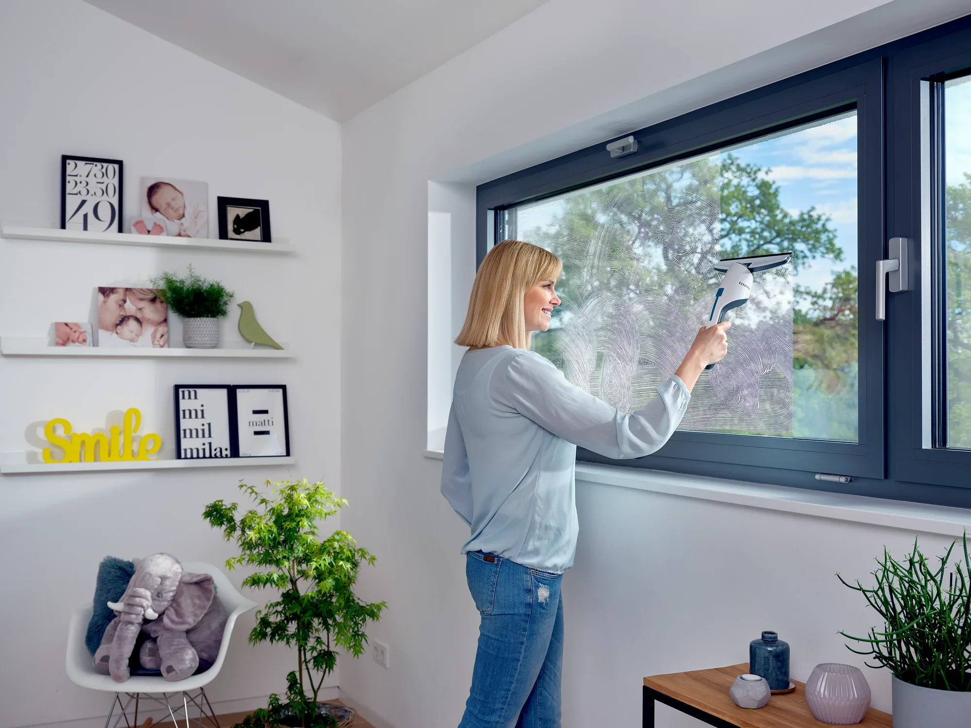 Eine Frau reinigt ein großes Fenster mit dem Nemo Fenstersauger. Im Hintergrund ist ein helles, modern eingerichtetes Zimmer mit Pflanzen und Dekorationen zu sehen.