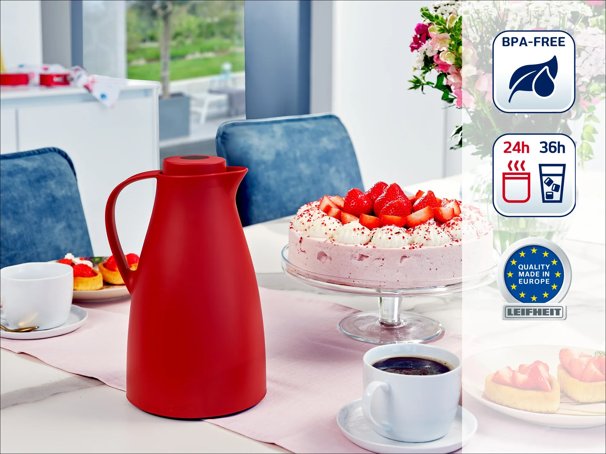 Een rode thermosfles staat op een gedekte tafel naast een aardbeientaart en koffiekopjes. Op de achtergrond is een moderne keuken te zien. De kan is BPA-vrij en houdt dranken 24 tot 36 uur warm of koud.