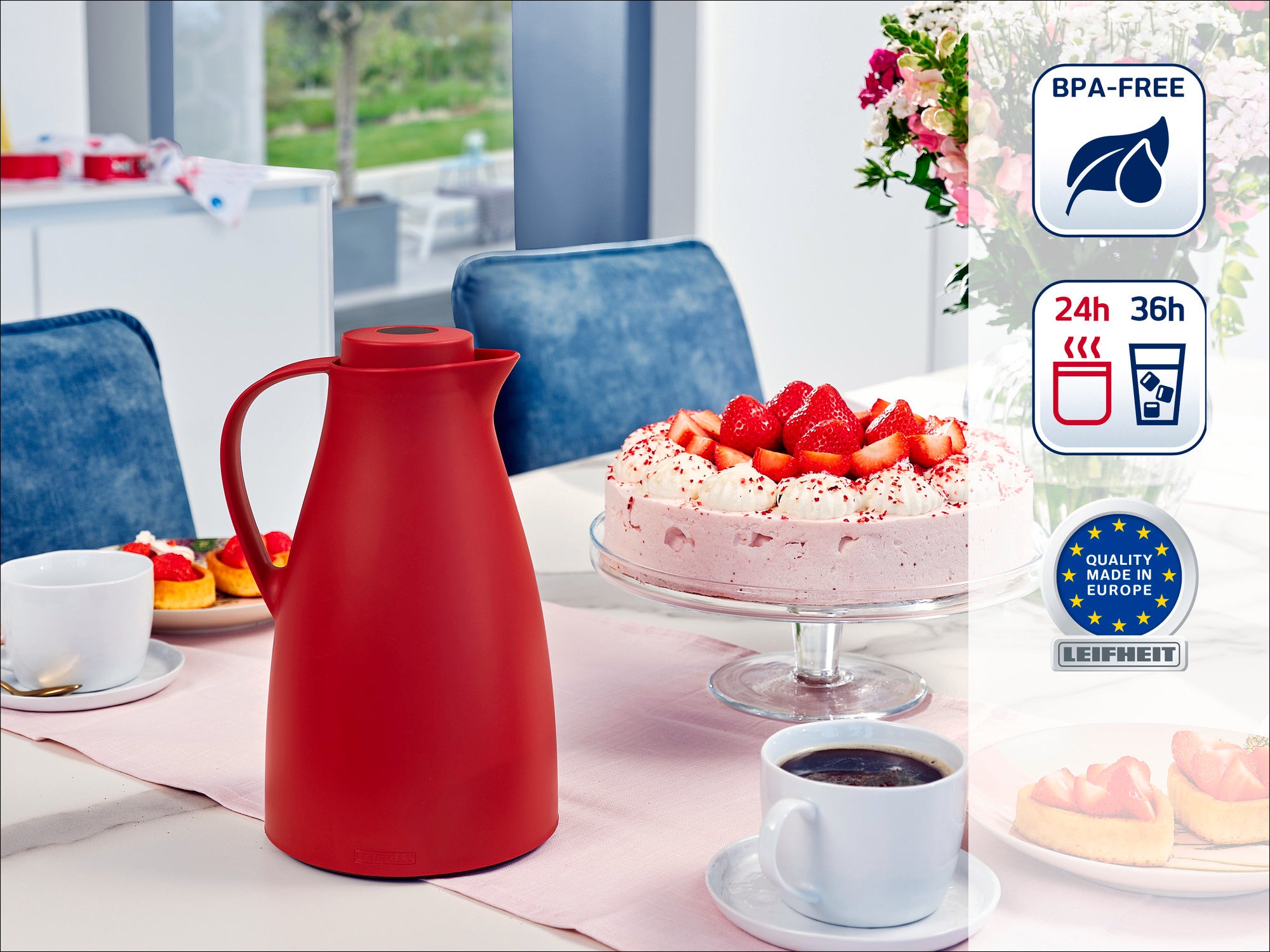 Eine rote Thermoskanne steht auf einem gedeckten Tisch neben einer Erdbeertorte und Kaffeetassen. Im Hintergrund ist eine moderne Küche zu sehen. Die Kanne ist BPA-frei und hält Getränke 24 bis 36 Stunden warm oder kalt.