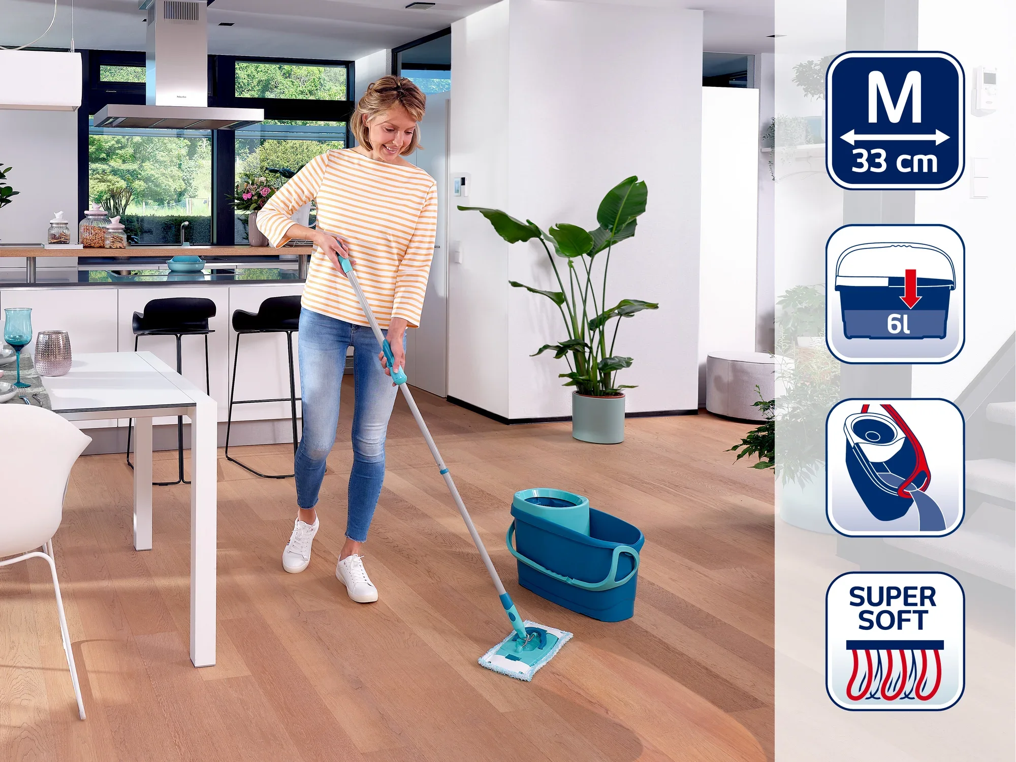Une femme nettoie le parquet d'une cuisine moderne avec une serpillière Leifheit. La serpillière a une tête de 33 cm de large et s'utilise avec un seau de 6 litres.