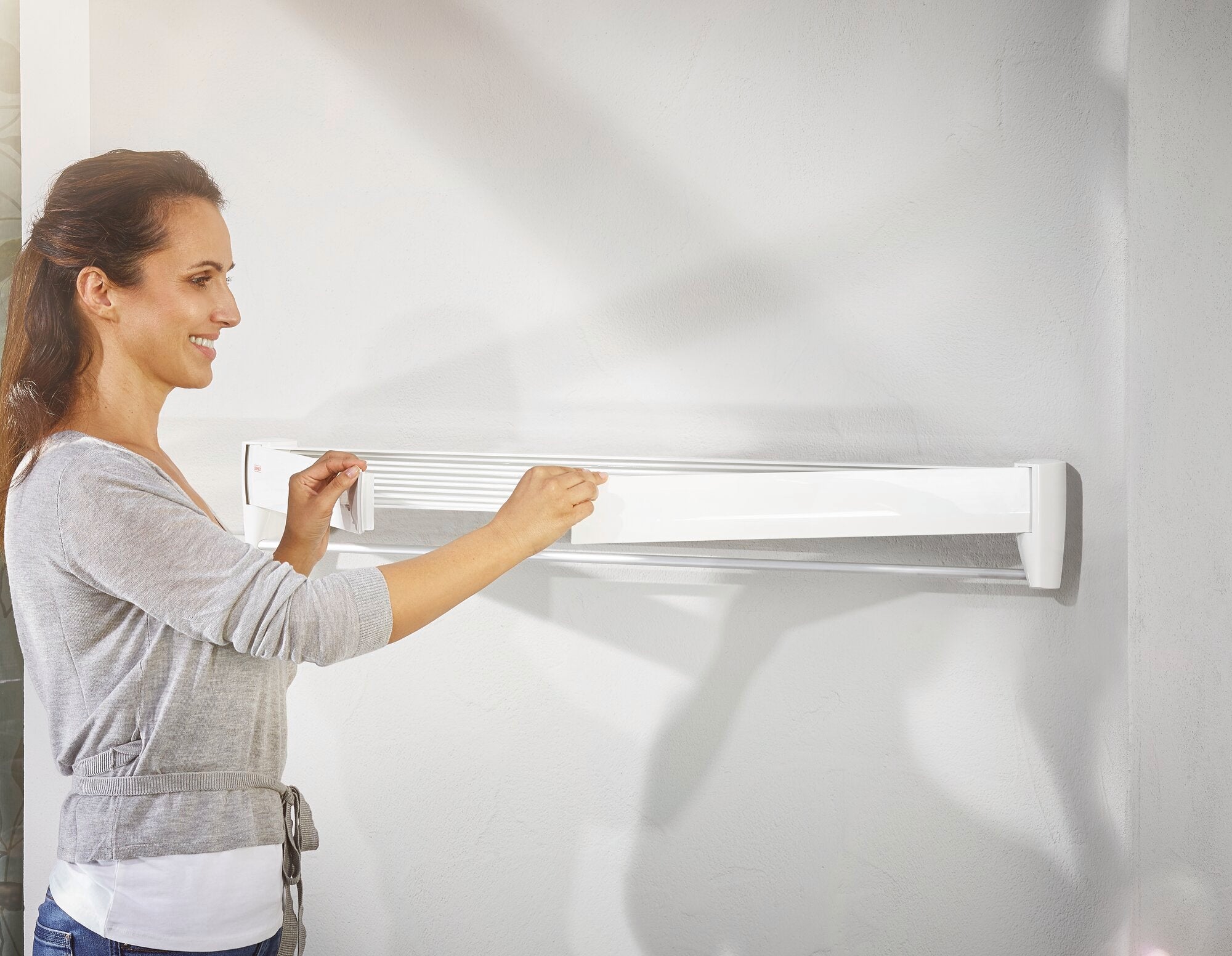 Eine Frau montiert den Wandtrockner Telegant 81 Protect Plus an einer Wand. Der Trockner ist kompakt und platzsparend, ideal für kleine Räume.