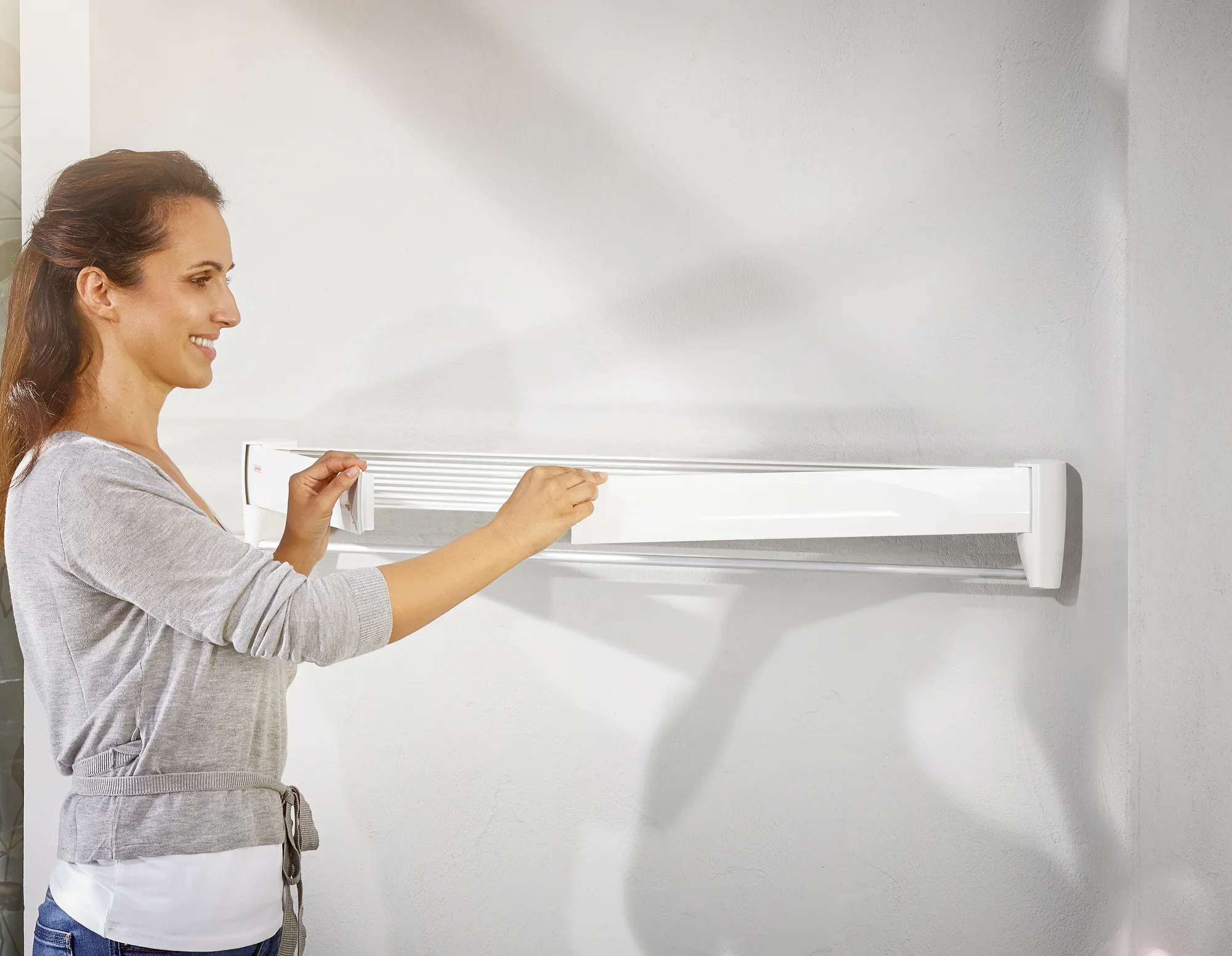 Een vrouw monteert de Telegant 81 Protect Plus wanddroger aan een muur. De droger is compact en ruimtebesparend, ideaal voor kleine ruimtes.