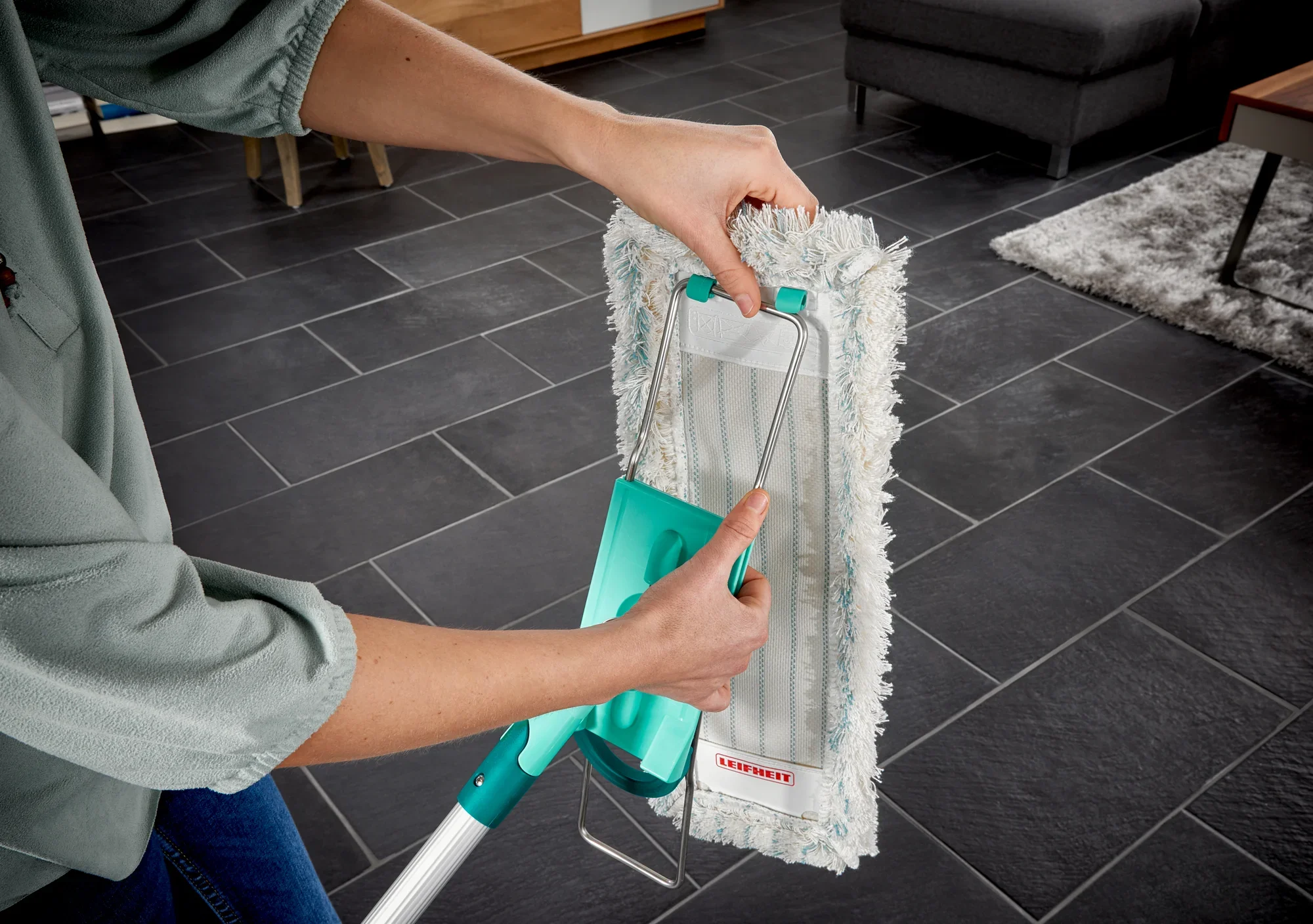 Una persona utilizza il lavapavimenti Profi XL su un pavimento piastrellato scuro. Il lavapavimenti ha un manico verde e un panno assorbente bianco che garantisce una pulizia accurata.
