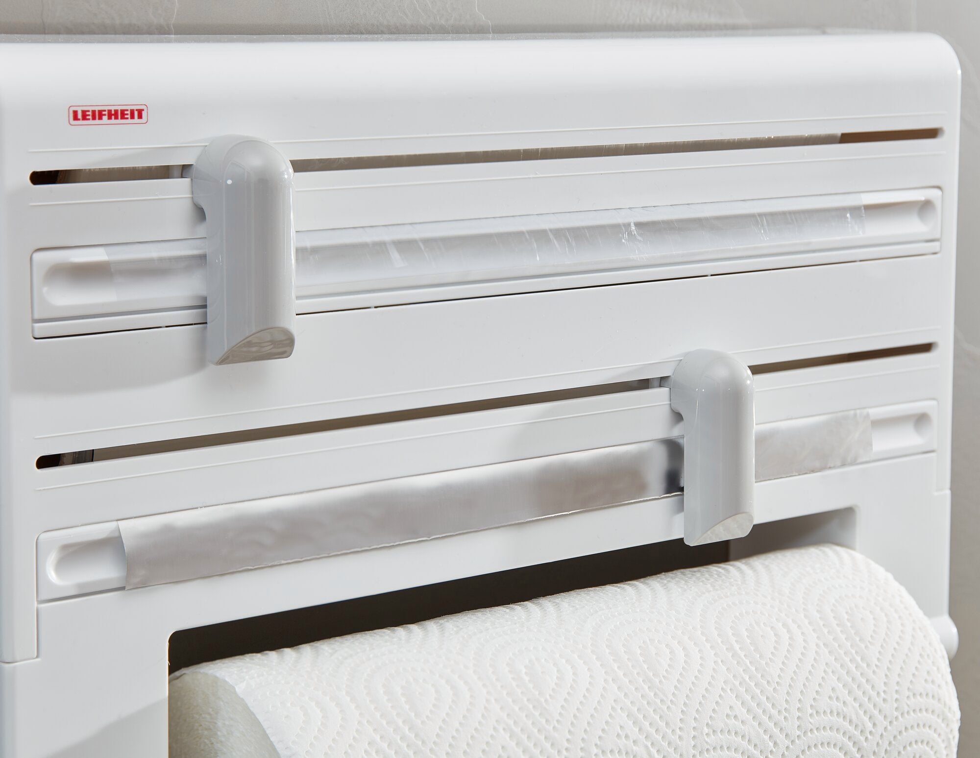 Un soporte de rollo de pared de Leifheit, modelo Parat, montado en la pared. El soporte ofrece espacio para rollos de cocina y film transparente, con dispositivos de corte de fácil acceso.