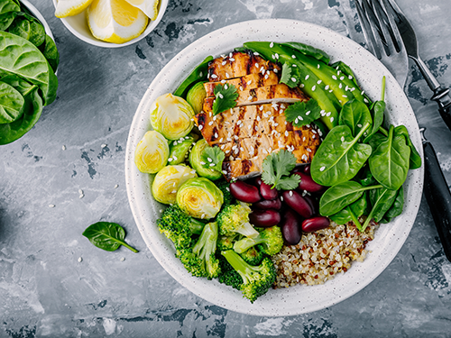 Eine Quinoa-Bowl mit Brokkoli, Rosenkohl, Kidneybohnen und Spinat, garniert mit Sesam und Koriander.