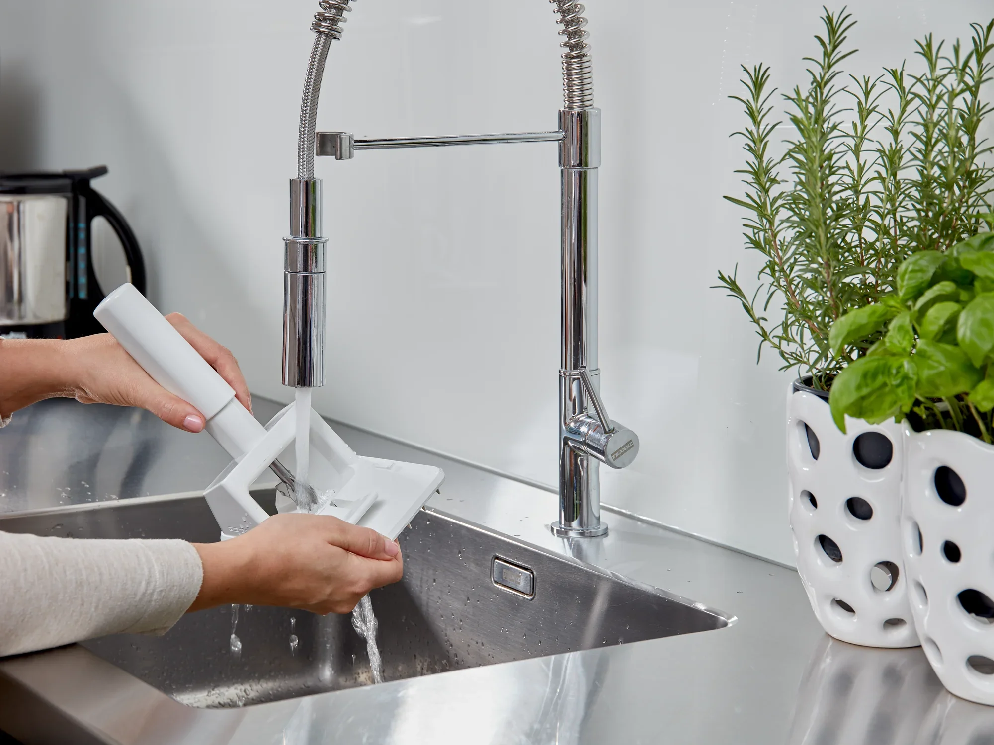 Osoba czyści drylownicę do śliwek pod bieżącą wodą w nowoczesnej kuchni. Destoner jest biały i jest płukany pod błyszczącym kranem.
