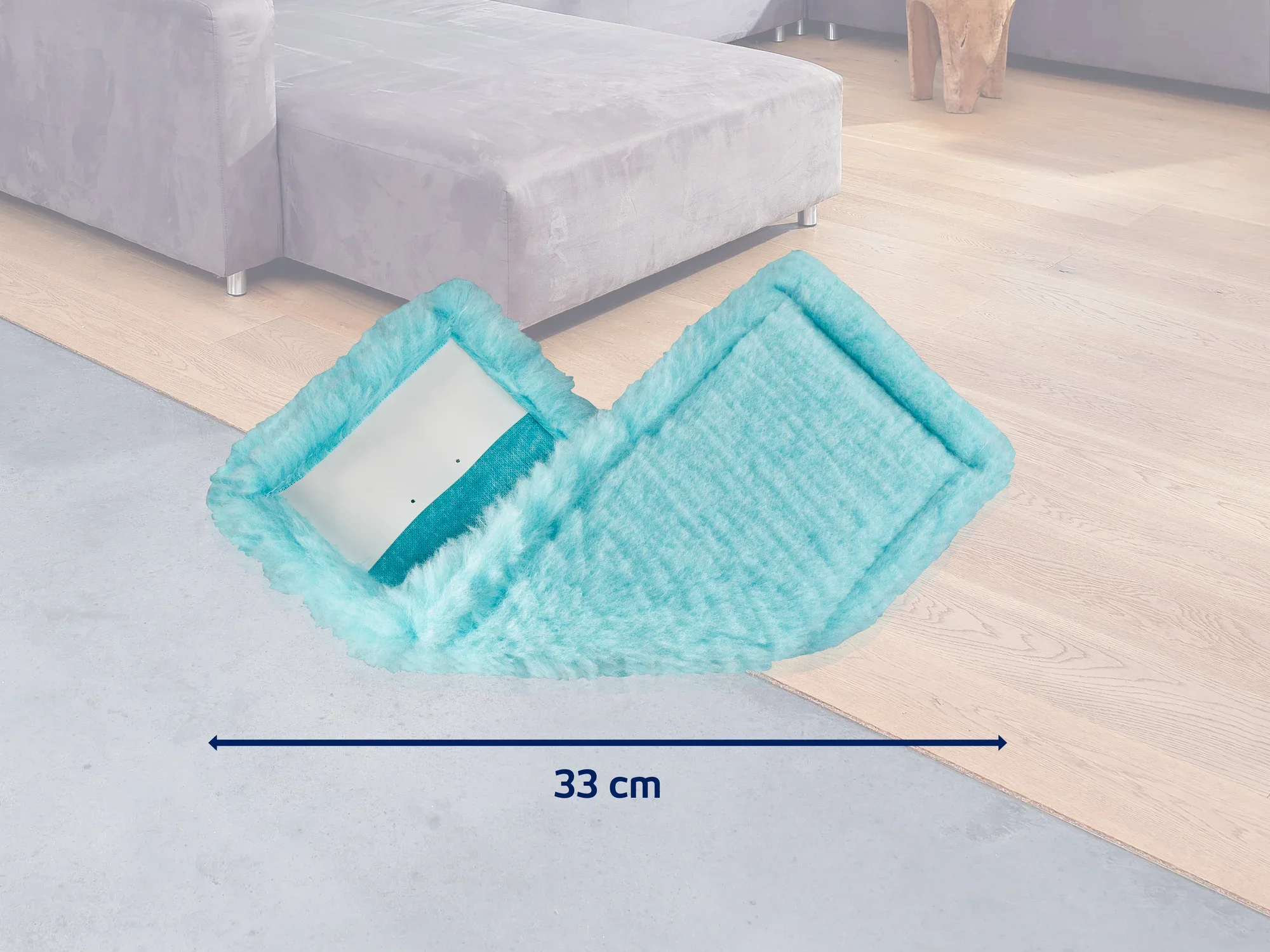 Ein türkisfarbener Wischmopp mit einer Breite von 33 cm liegt auf einem Holzboden neben einem grauen Sofa. Der Mopp ist ideal für die gründliche Reinigung von Böden.