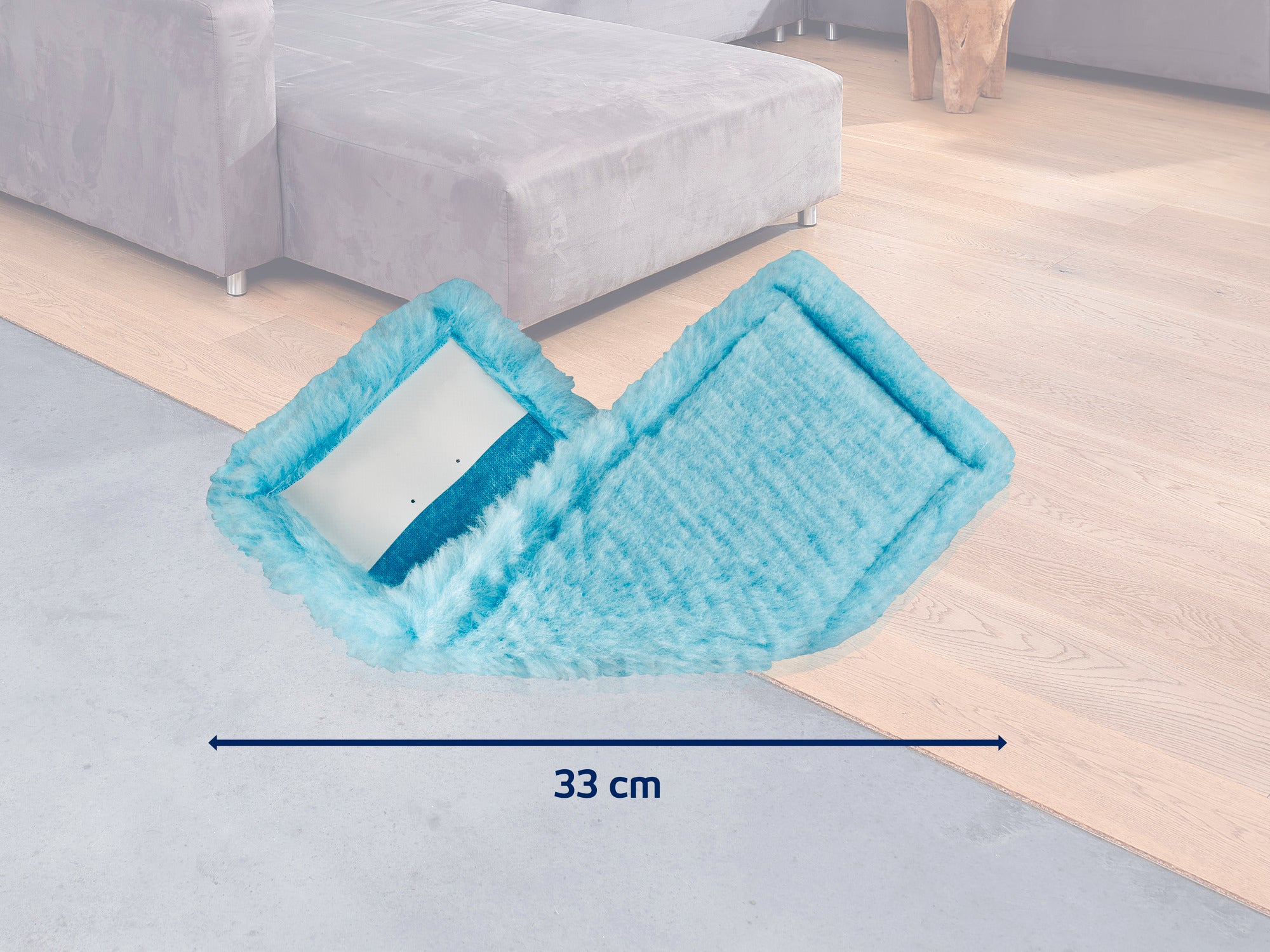 Een turquoise mop met een breedte van 33 cm ligt op een houten vloer naast een grijze bank. De mop is ideaal voor het grondig reinigen van vloeren.