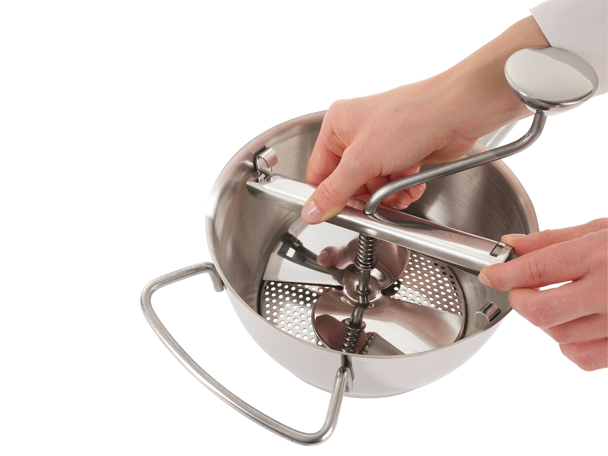 Food mill in use: A person turns the handle of a stainless steel food mill. The mill has a sturdy handle and a fine sieve, ideal for pureeing food.