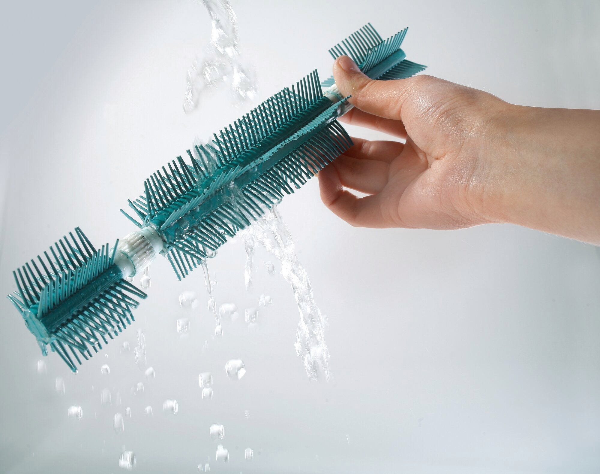 Eén hand houdt de Regulus Supra veegmachine onder stromend water om de blauwe borstelharen schoon te maken. De veegmachine is ideaal voor een grondige en eenvoudige reiniging.