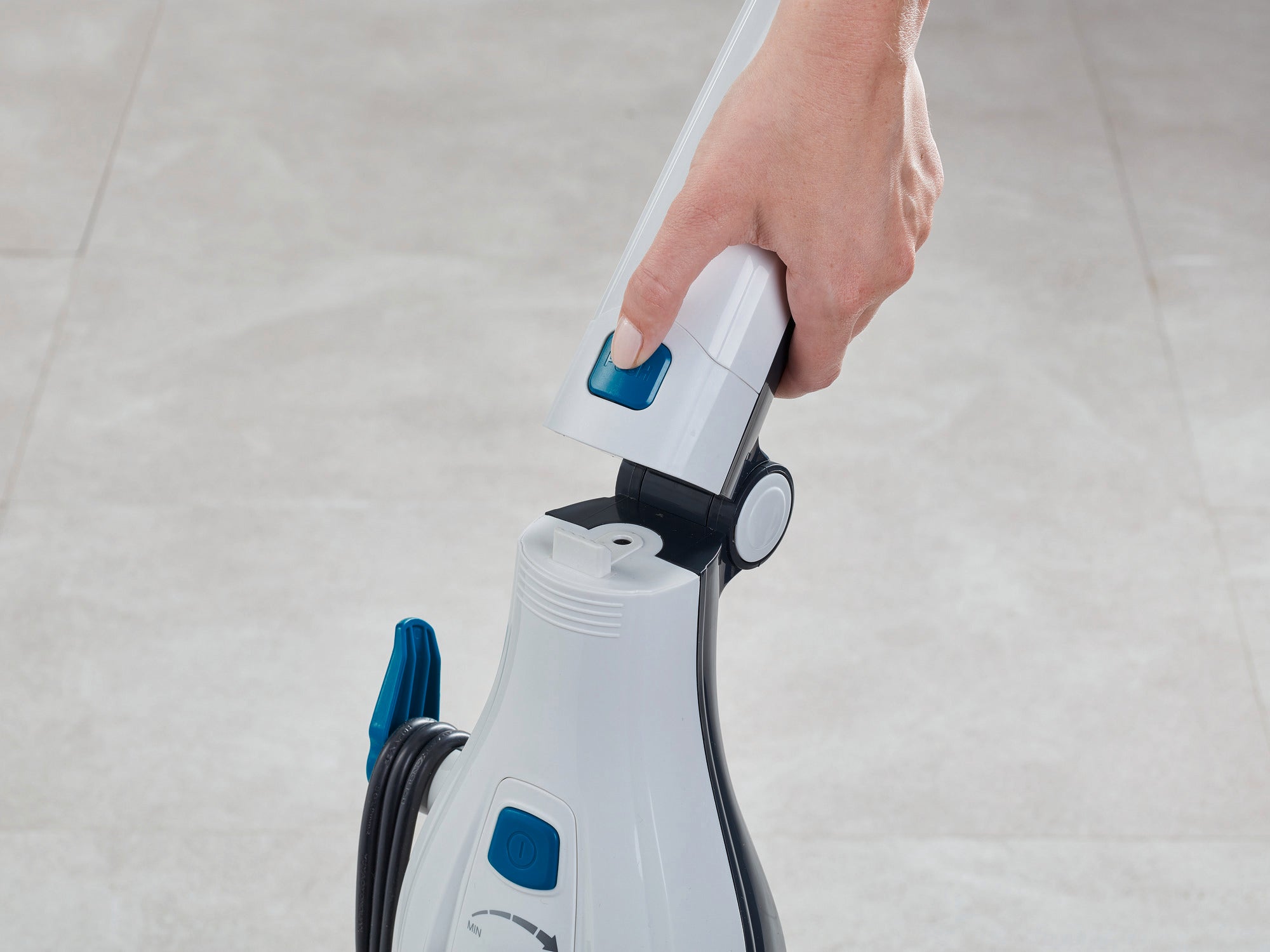 Clean Tenso stoomreiniger in gebruik. Eén hand houdt het handvat van het apparaat vast, dat op een lichtgekleurde vloer staat. De stoomreiniger is wit met blauwe accenten.