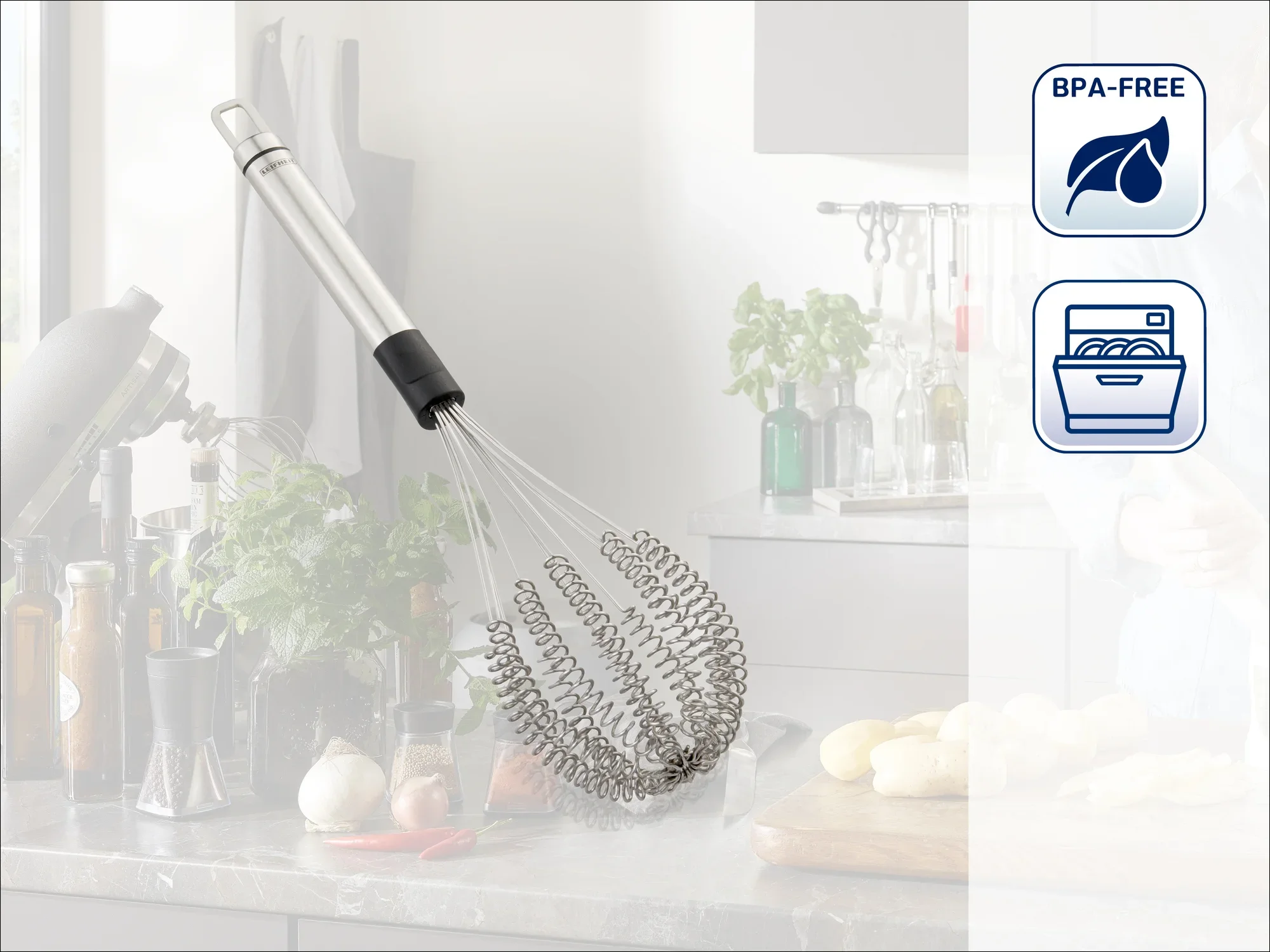 Trzepaczka ze stali nierdzewnej spoczywa na nowoczesnym blacie kuchennym. W tle widoczne są świeże składniki i przybory kuchenne. Na zdjęciu widoczne są symbole oznaczające brak BPA i możliwość mycia w zmywarce.