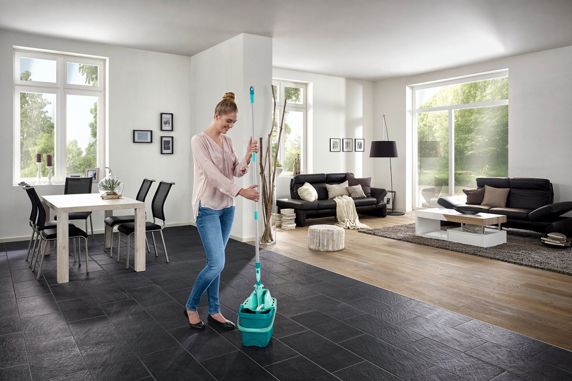 Eine Frau benutzt den Bodenwischer Combi M in einem modernen Wohnzimmer. Der Wischer hat einen türkisfarbenen Eimer und ist ideal für die Reinigung großer Flächen.