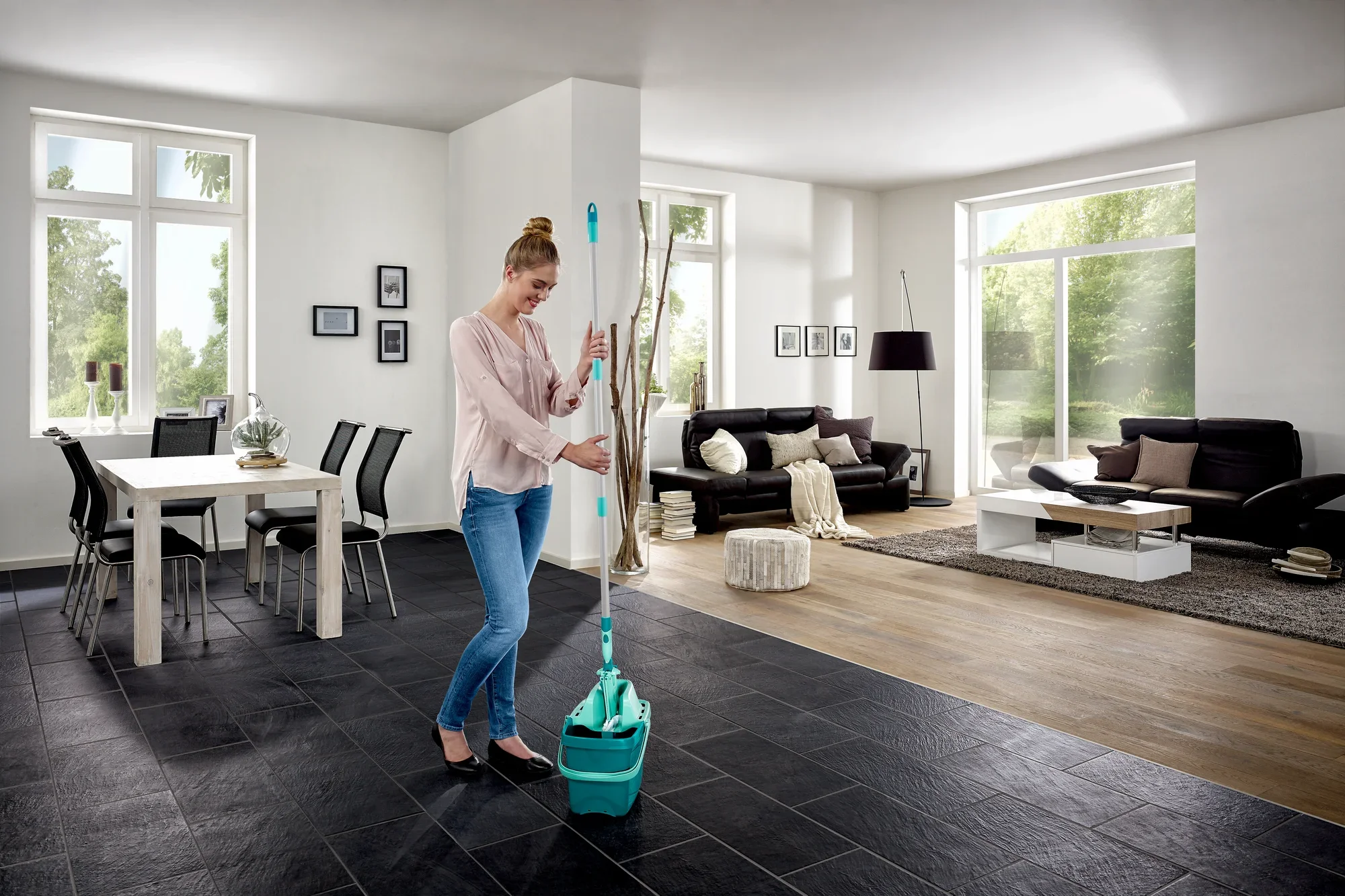 Eine Frau benutzt den Bodenwischer Combi M in einem modernen Wohnzimmer. Der Wischer hat einen türkisfarbenen Eimer und ist ideal für die Reinigung großer Flächen.
