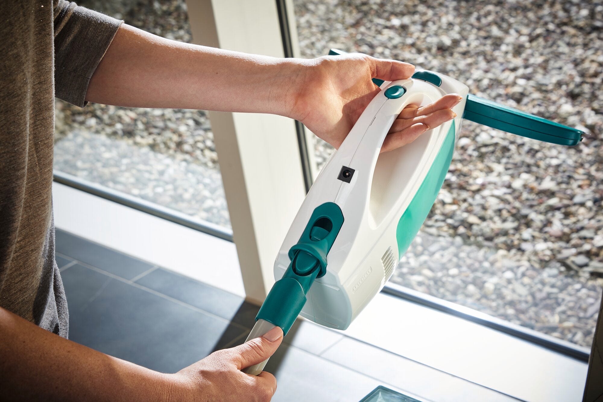 Un aspirateur pour vitres Dry and Clean est tenu à la main et utilisé pour nettoyer une fenêtre. L'appareil est compact et ergonomique, idéal pour un nettoyage sans traces.