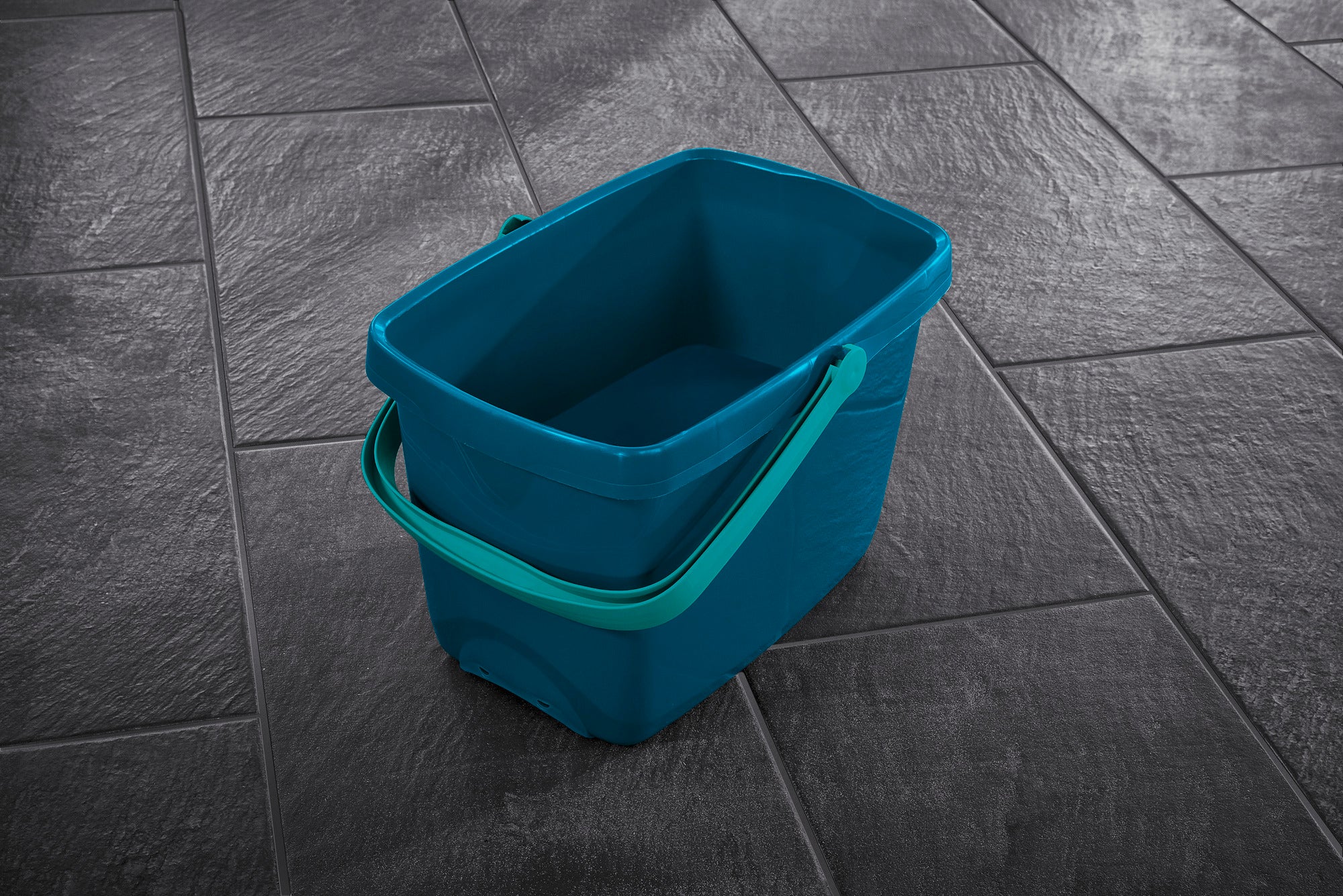 Un secchio blu con manico verde poggia su un pavimento piastrellato scuro. Il secchio è rettangolare e offre spazio sufficiente per le pulizie. Ideale per l'uso con il sistema Profi XL.