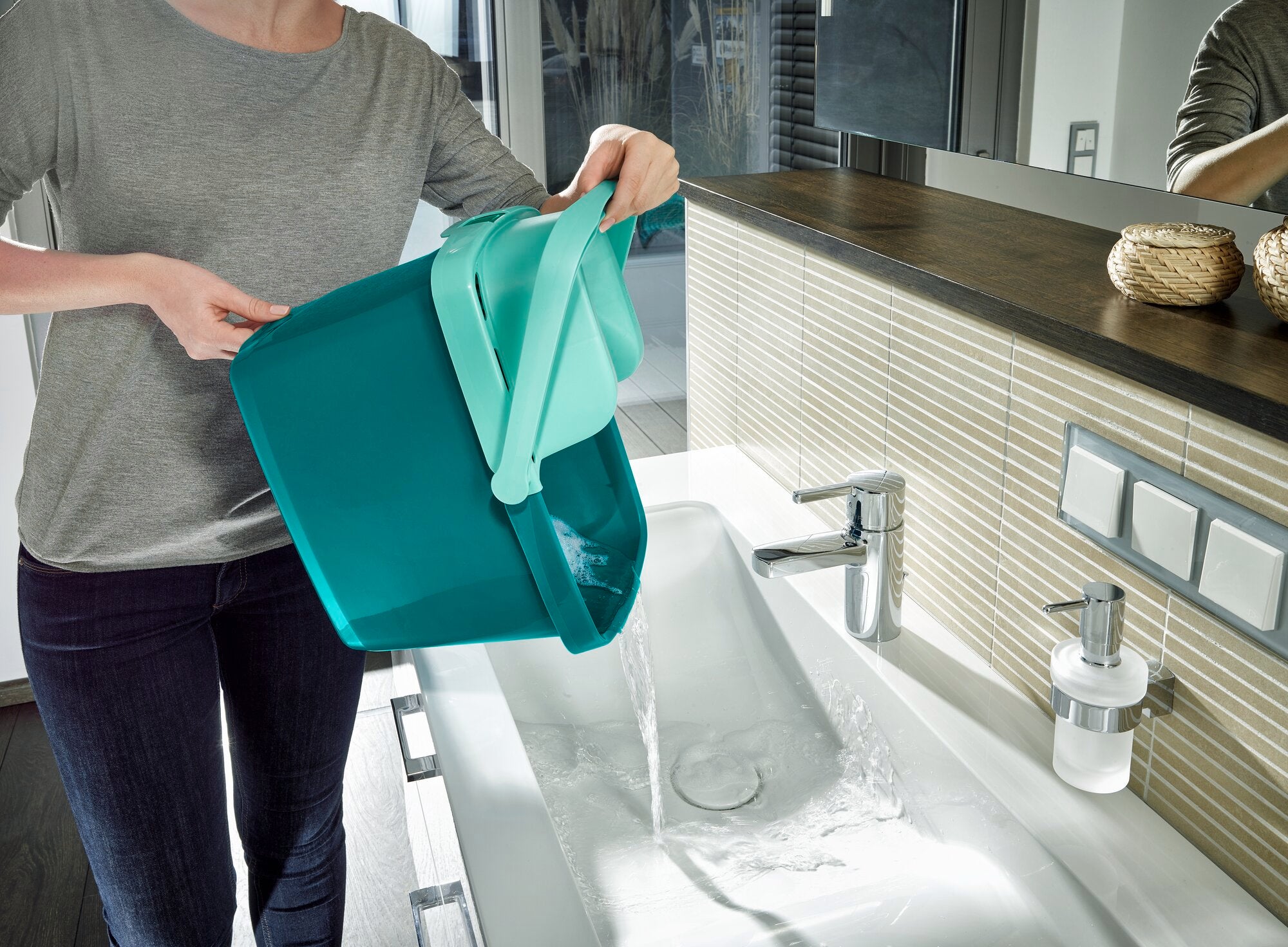 Eine Person leert einen Eimer mit Wasser in ein Waschbecken. Der Eimer gehört zum Bodenwischer-Set Combi M, das für effiziente Reinigung und einfache Handhabung bekannt ist.