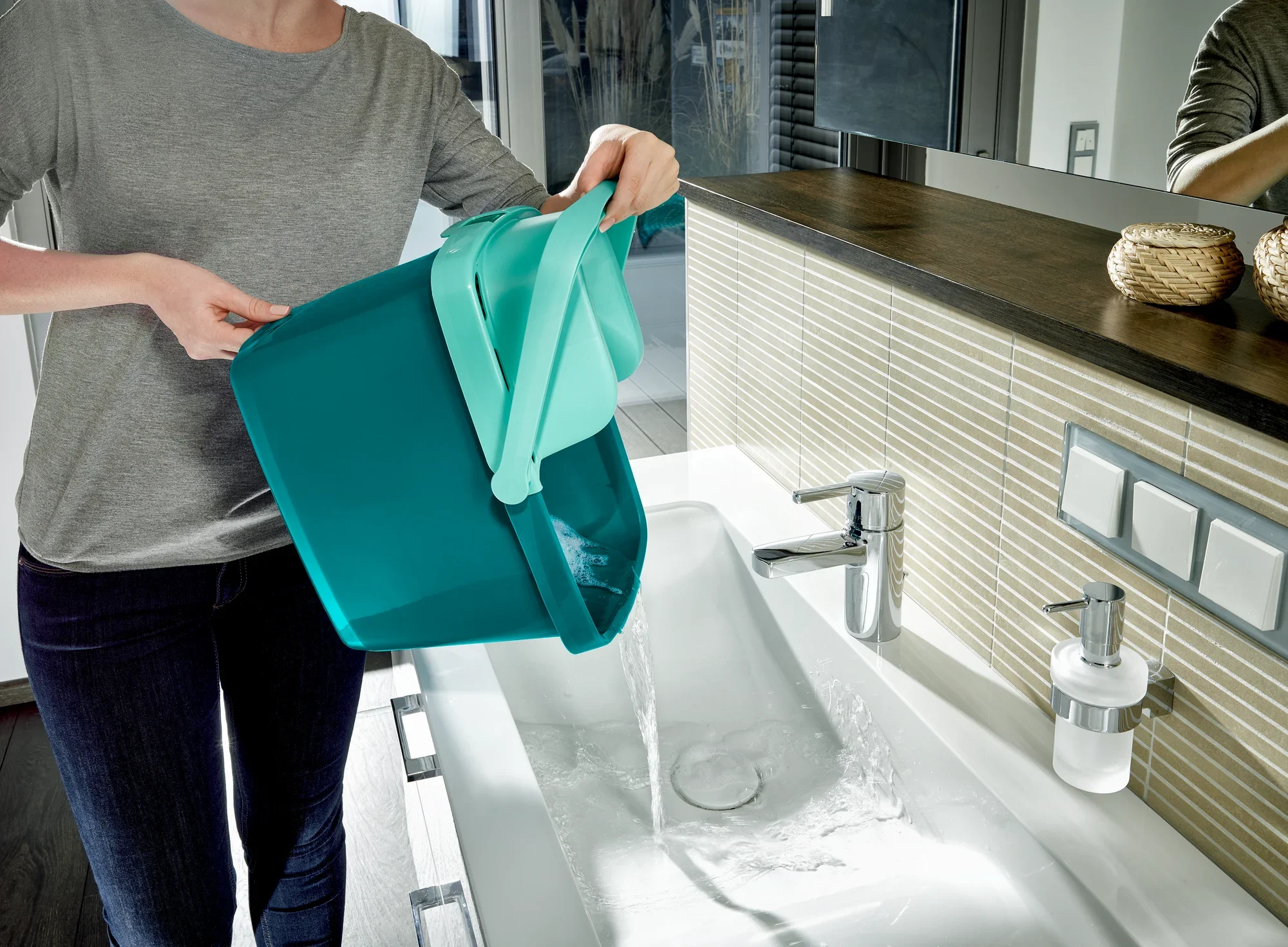 Eine Person leert einen Eimer mit Wasser in ein Waschbecken. Der Eimer gehört zum Bodenwischer-Set Combi M, das für effiziente Reinigung und einfache Handhabung bekannt ist.