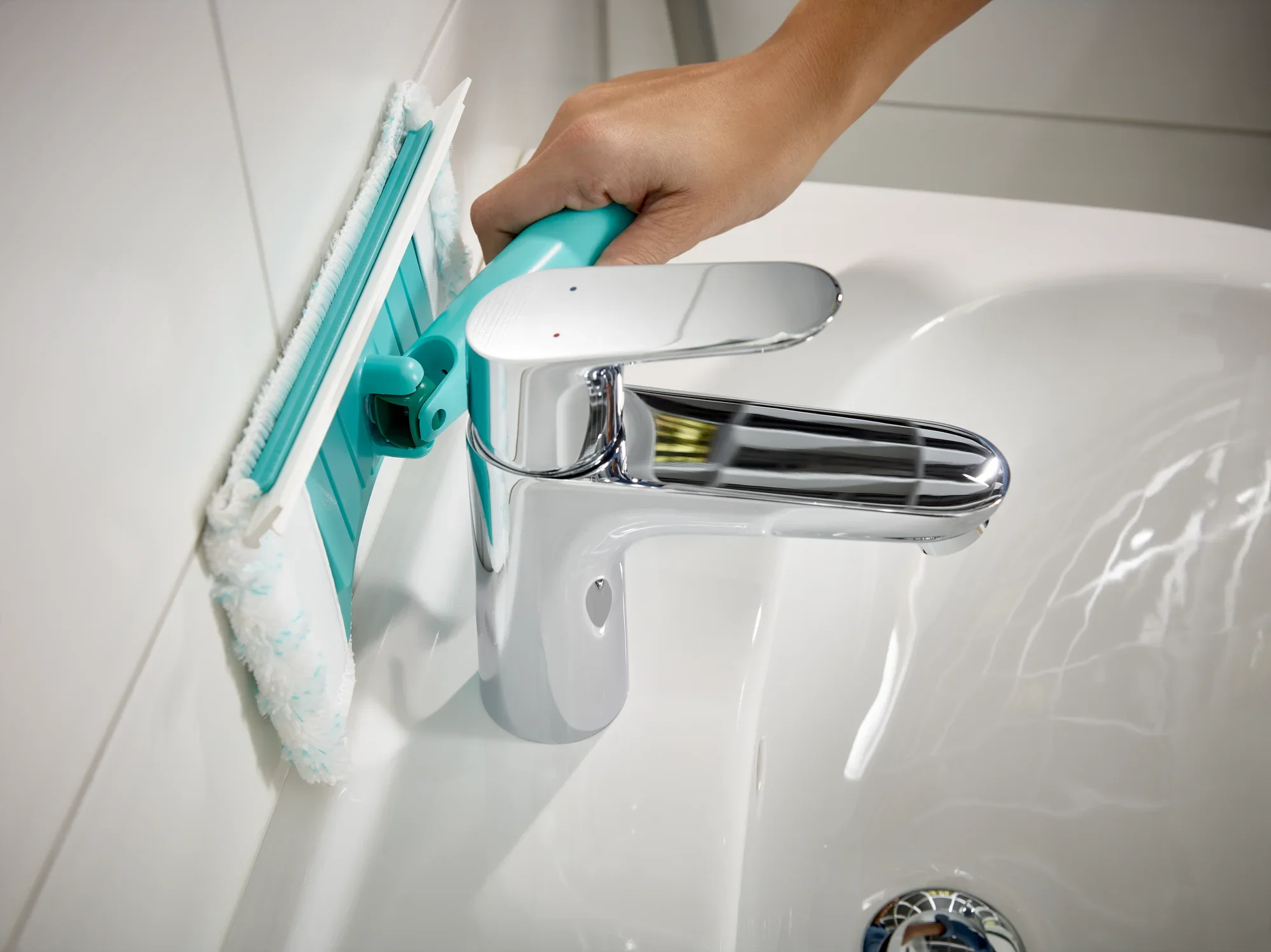 Ściągaczka do płytek i wanien Flexipad z teleskopowym uchwytem jest używana na ścianie w łazience. Ściągaczka ma niebieską nakładkę i jest prowadzona jedną ręką w celu wyczyszczenia płytek.