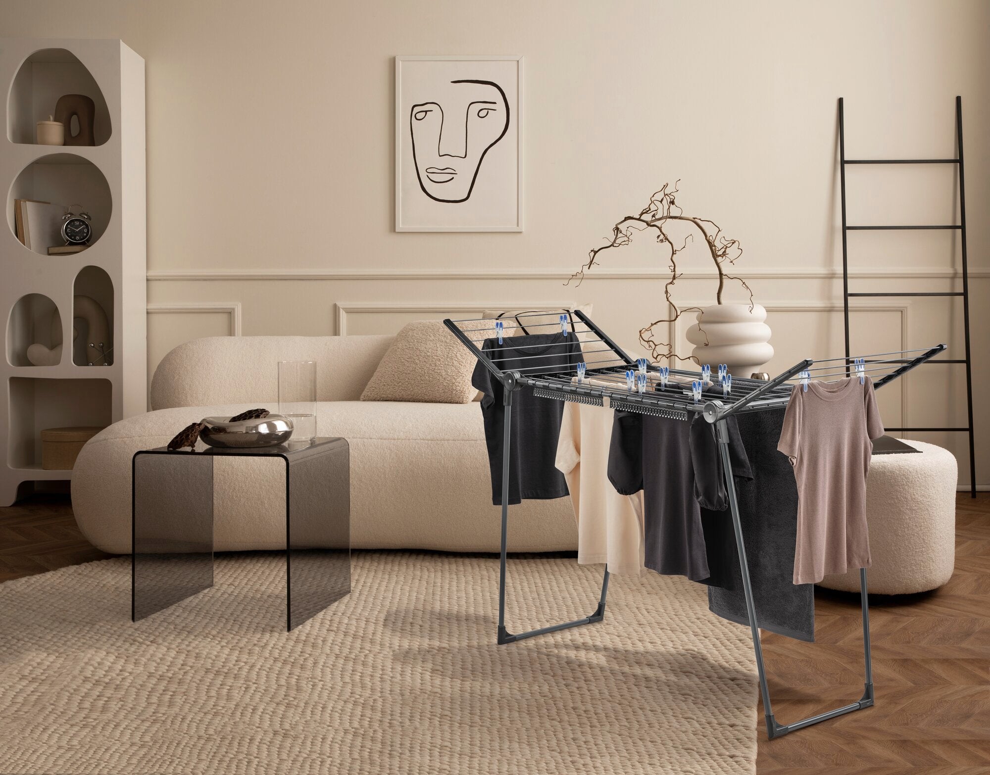 Pegasus 150 Solid Slim Black wasdroger in een stijlvolle woonkamer. De wasdroger is volgehangen met kleding en staat op een vloerkleed voor een bank en een modern kunstwerk.