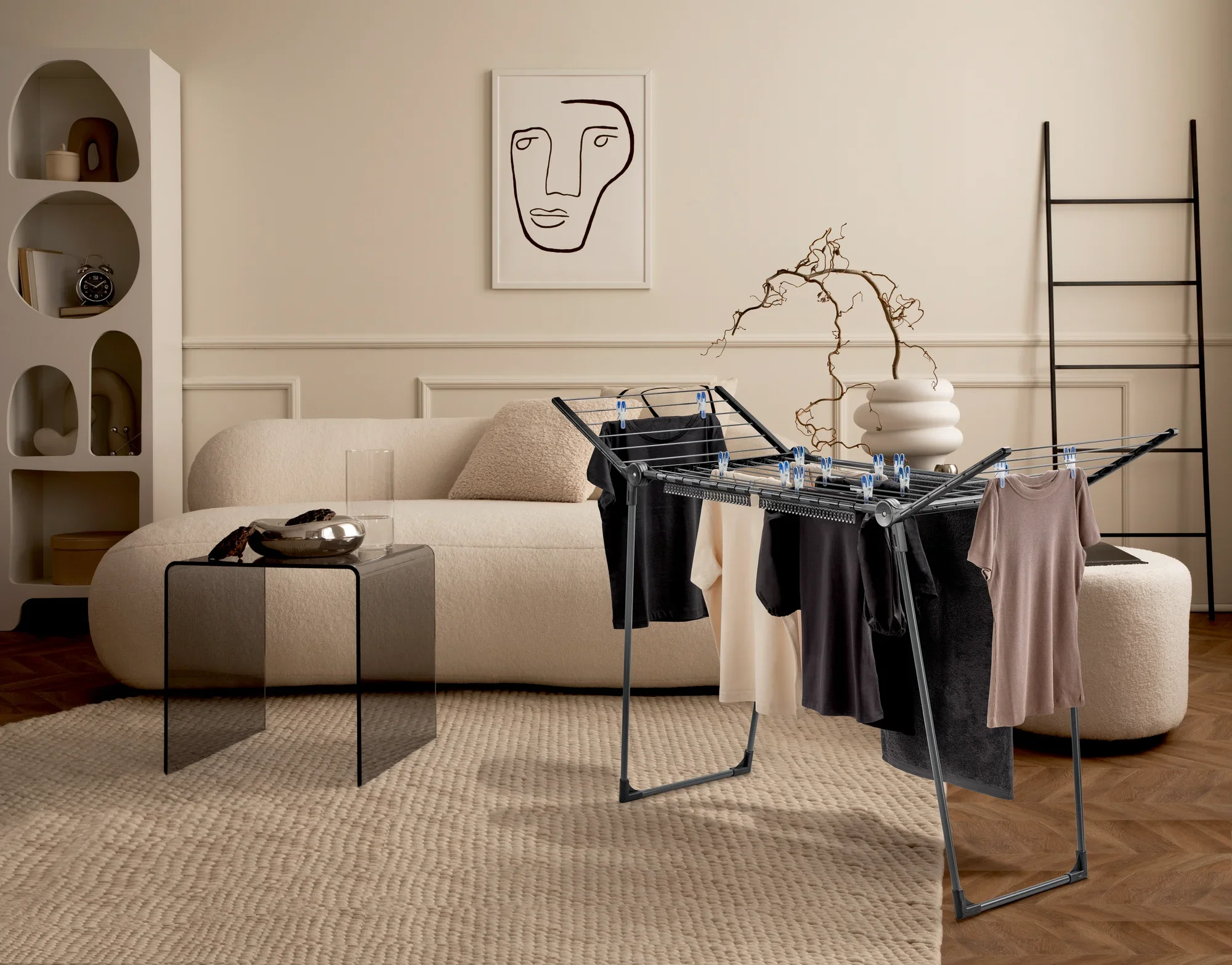 Suszarka bębnowa Pegasus 150 Solid Slim Black w stylowym salonie. Suszarka bębnowa jest zawieszona na ubraniach i stoi na dywanie przed sofą i nowoczesnym dziełem sztuki.