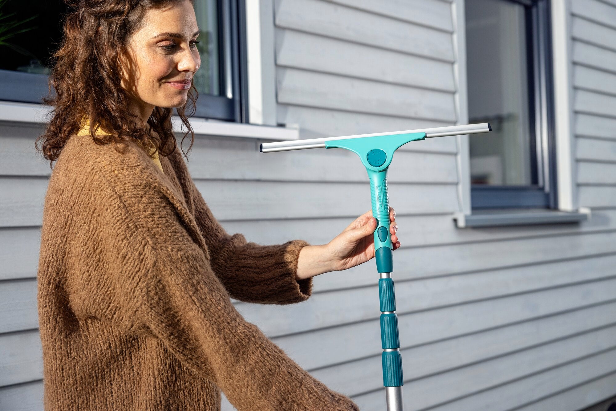 Kobieta używa ściągaczki 2 w 1 XL ProReach do mycia okien. Ściągaczka ma długi, regulowany uchwyt i szeroką powierzchnię wycierania, co zapewnia wydajną pracę.
