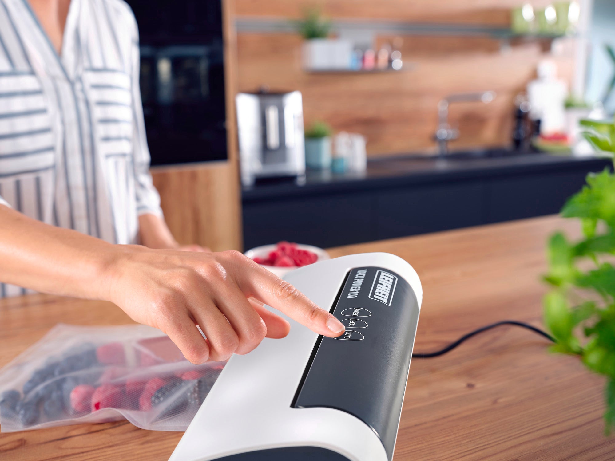 Una persona maneja la envasadora al vacío Vacu Power 100 en una cocina moderna. El aparato se utiliza para sellar alimentos en una bolsa con el fin de conservar su frescura.