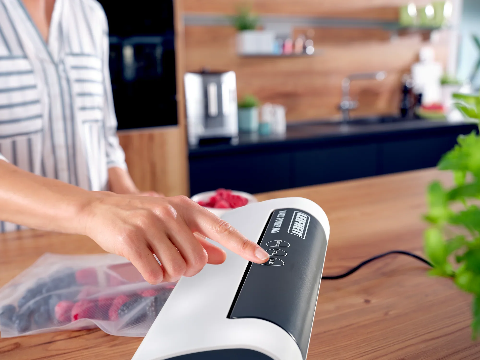 Osoba obsługuje zgrzewarkę próżniową Vacu Power 100 w nowoczesnej kuchni. Urządzenie służy do zamykania żywności w torebkach w celu zachowania świeżości.