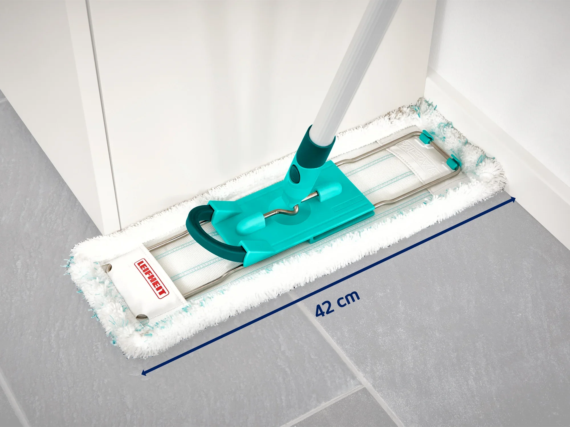 A Leifheit floor mop with a 42 cm wide mop head lies on a grey tiled floor. The mop has a turquoise handle and is ideal for cleaning corners.