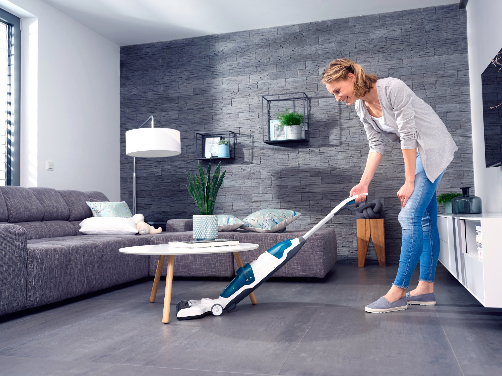 Eine Frau benutzt den Regulus Aqua PowerVac, um den Boden in einem modernen Wohnzimmer zu reinigen. Der Staubsauger ist kabellos und effizient für die tägliche Reinigung.