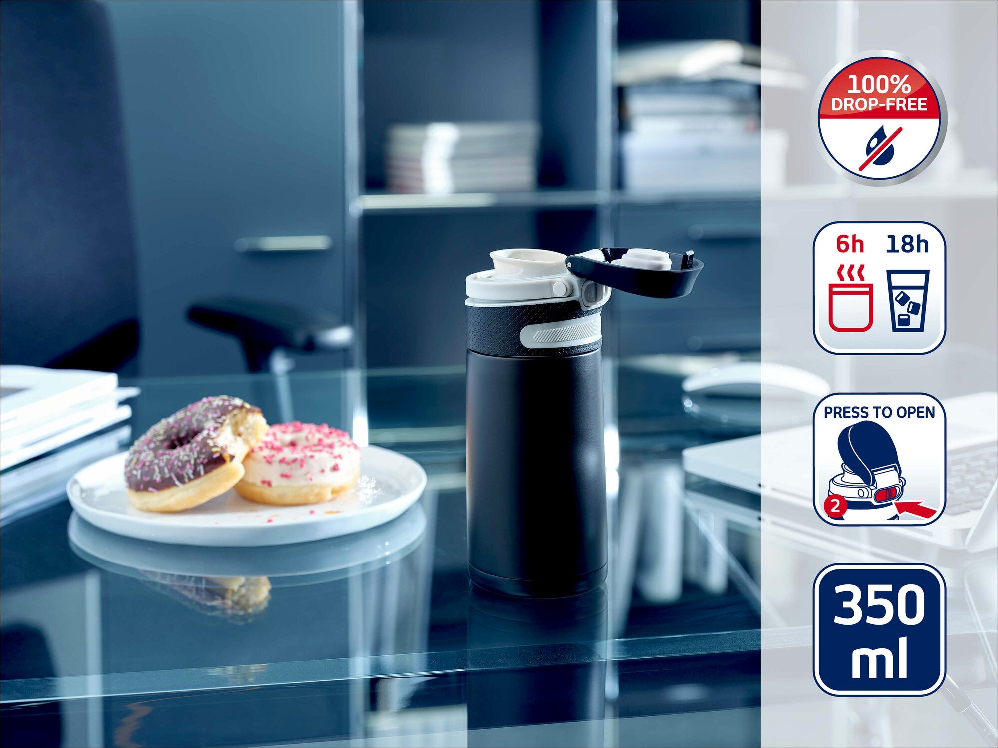 Leifheit Isolierbecher 350 ml in Schwarz auf einem Glastisch im Büro, mit geöffnetem Trinkverschluss neben einem Teller mit zwei Donuts; Symbolhinweise zeigen 100 % auslaufsicher, 6 h heiß, 18 h kalt und komfortables Öffnen per Knopfdruck.