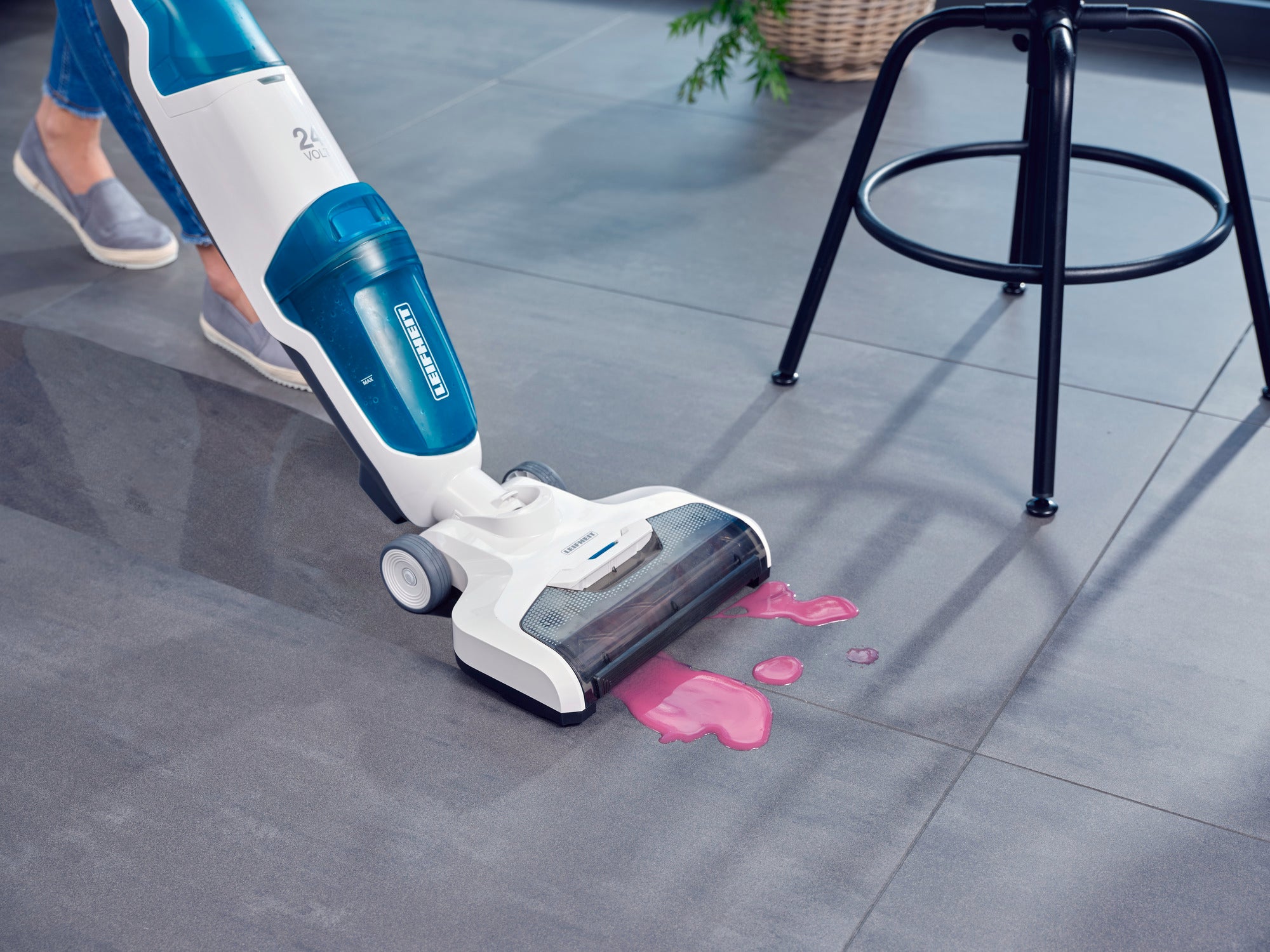 Ein Regulus Aqua PowerVac Staubsauger reinigt einen Boden, indem er eine verschüttete Flüssigkeit aufnimmt. Der Staubsauger ist in einem modernen, hellen Raum im Einsatz.