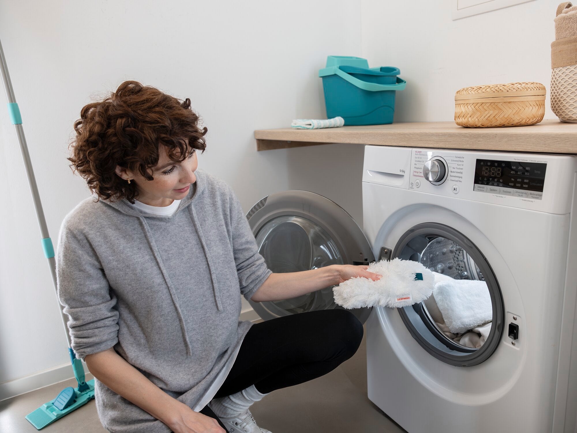 Een vrouw stopt de SUPERDUSTER plumeau in de wasmachine. De plumeau is wit en handig, ideaal voor moeilijk bereikbare plaatsen. Op de achtergrond zijn schoonmaakspullen te zien.