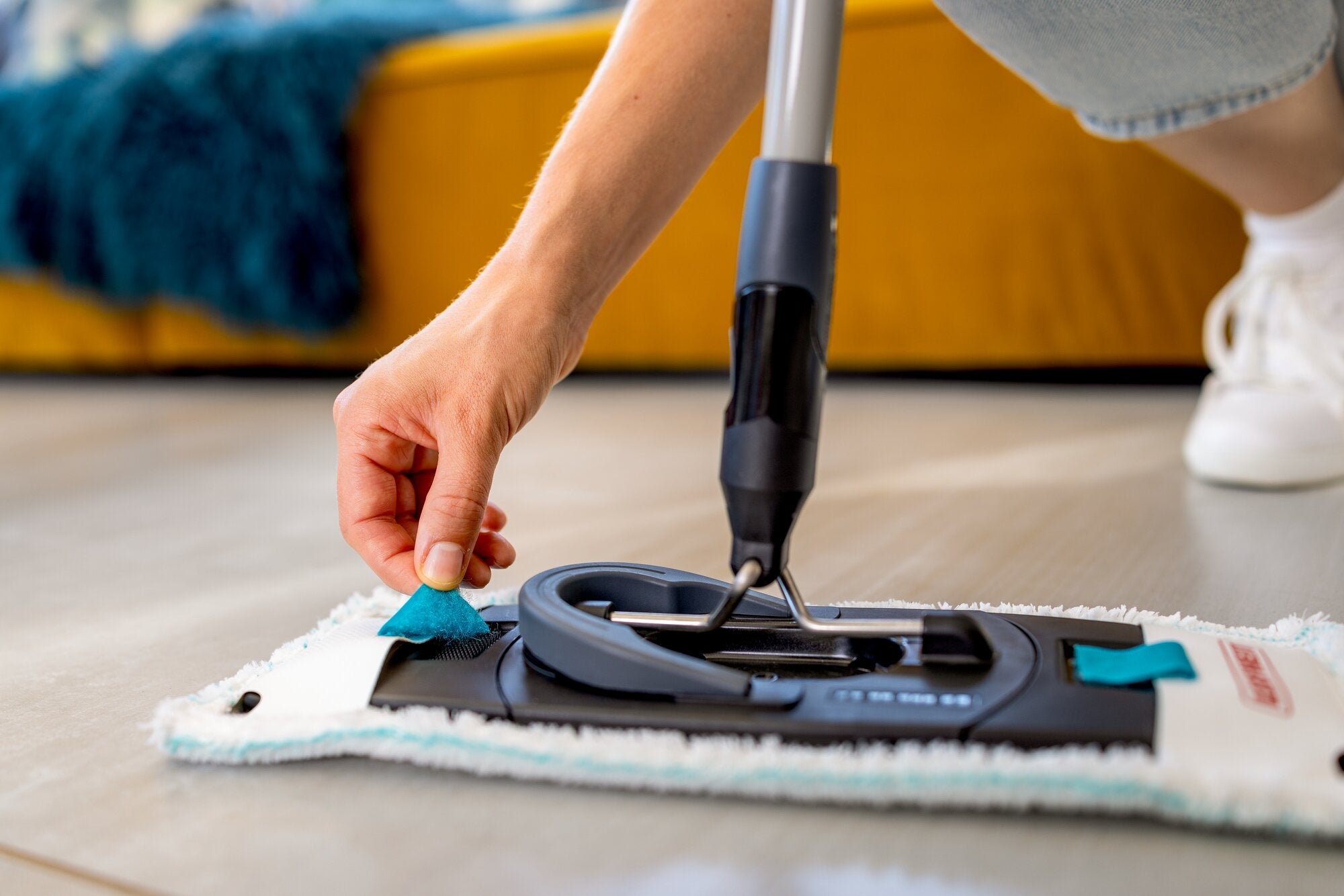 Leifheit Set CLEAN TWIST M Ergo Black mit flachem Bodenwischer und Mikrofaserbezug im Einsatz auf glattem Boden, eine Hand befestigt den Bezug per Klicksystem für komfortables und gründliches Wischen.