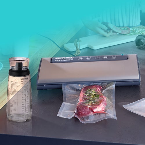 Een keuken met een vacuuemmachine, verse kruiden, gesneden vlees en groenten.