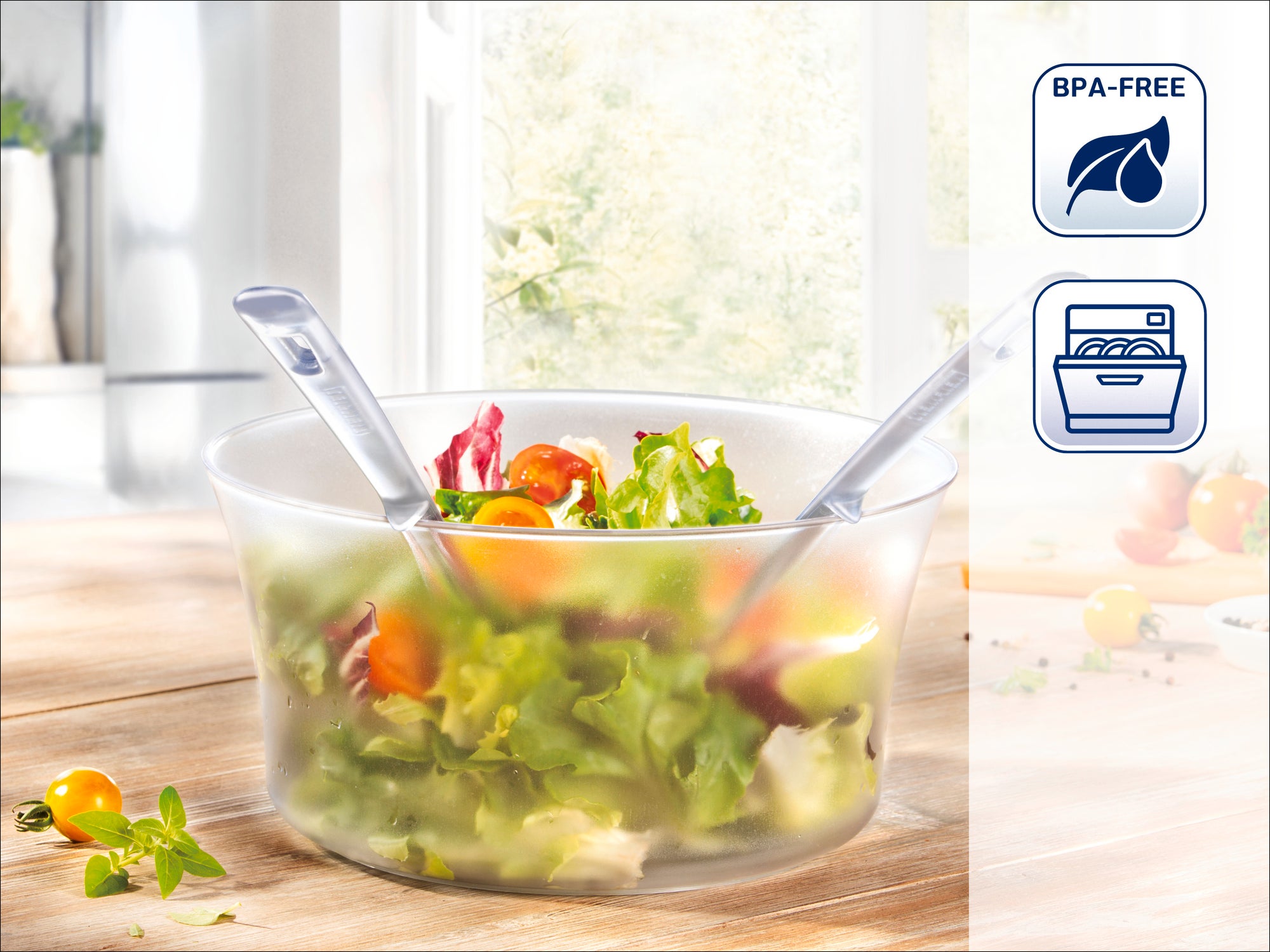 Eine transparente Salatschüssel mit frischem Salat und zwei Servierlöffeln. Im Hintergrund eine helle Küche. Symbole zeigen BPA-frei und spülmaschinengeeignet an.