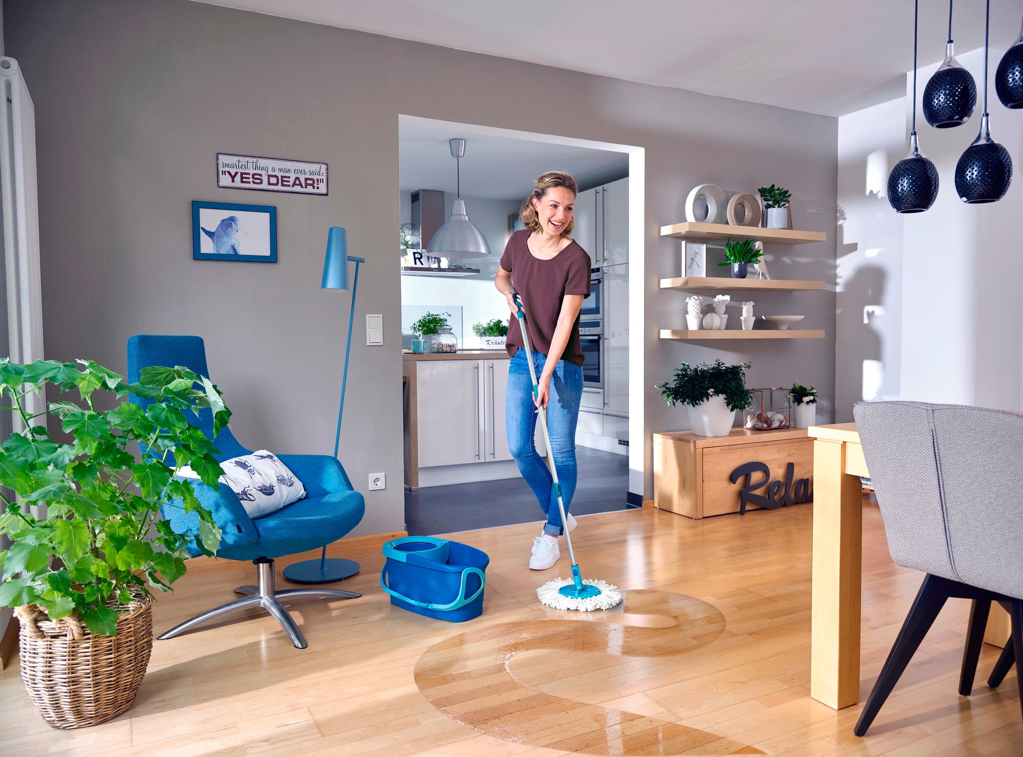 Une femme nettoie le parquet d'un salon moderne avec le kit de nettoyage CLEAN TWIST. À l'arrière-plan, on aperçoit des meubles élégants et des plantes qui créent une atmosphère chaleureuse.