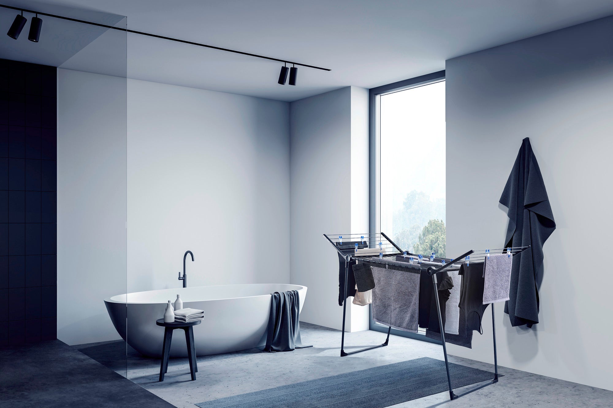 Une pièce moderne et minimaliste avec un sèche-linge sur pied Pegasus 180 Solid. Le sèche-linge est chargé de vêtements et se trouve à côté d'une baignoire îlot.