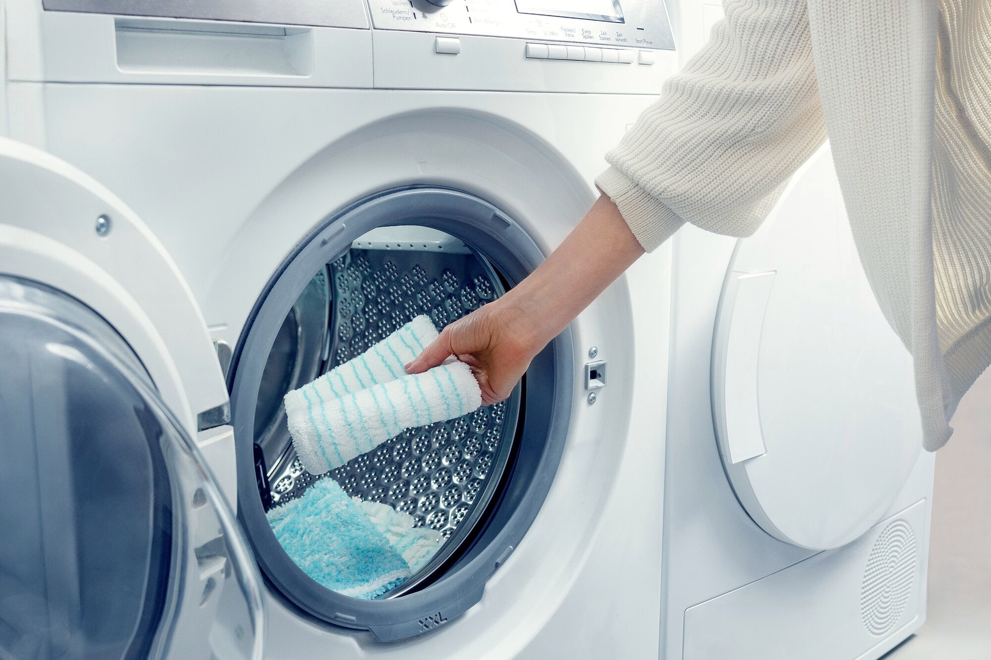 A person puts a mop cover in a modern washing machine. The image shows that the mop cover is washable.