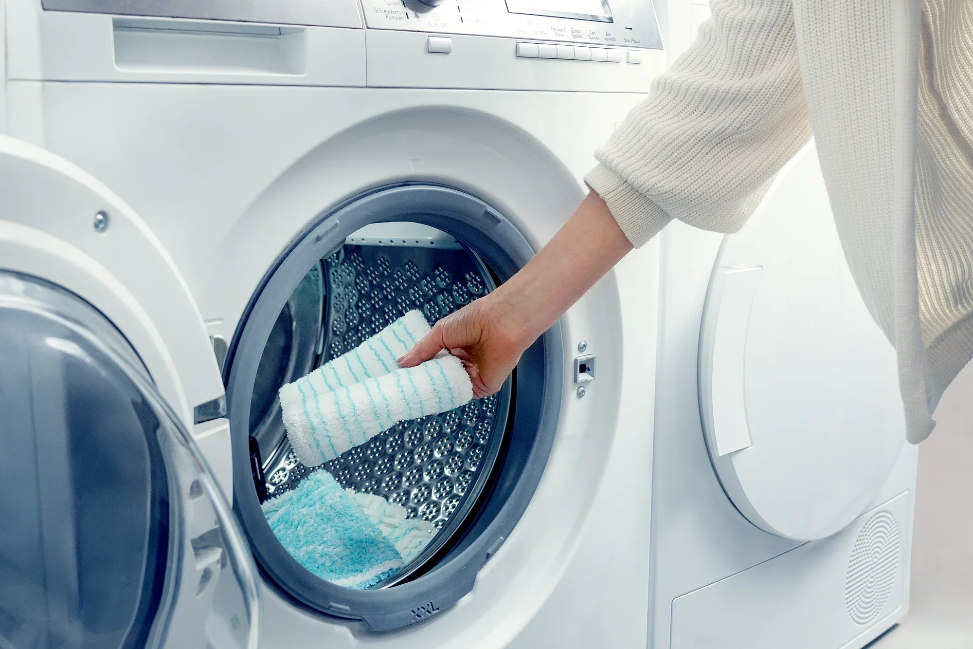 A person puts a mop cover in a modern washing machine. The image shows that the mop cover is washable.