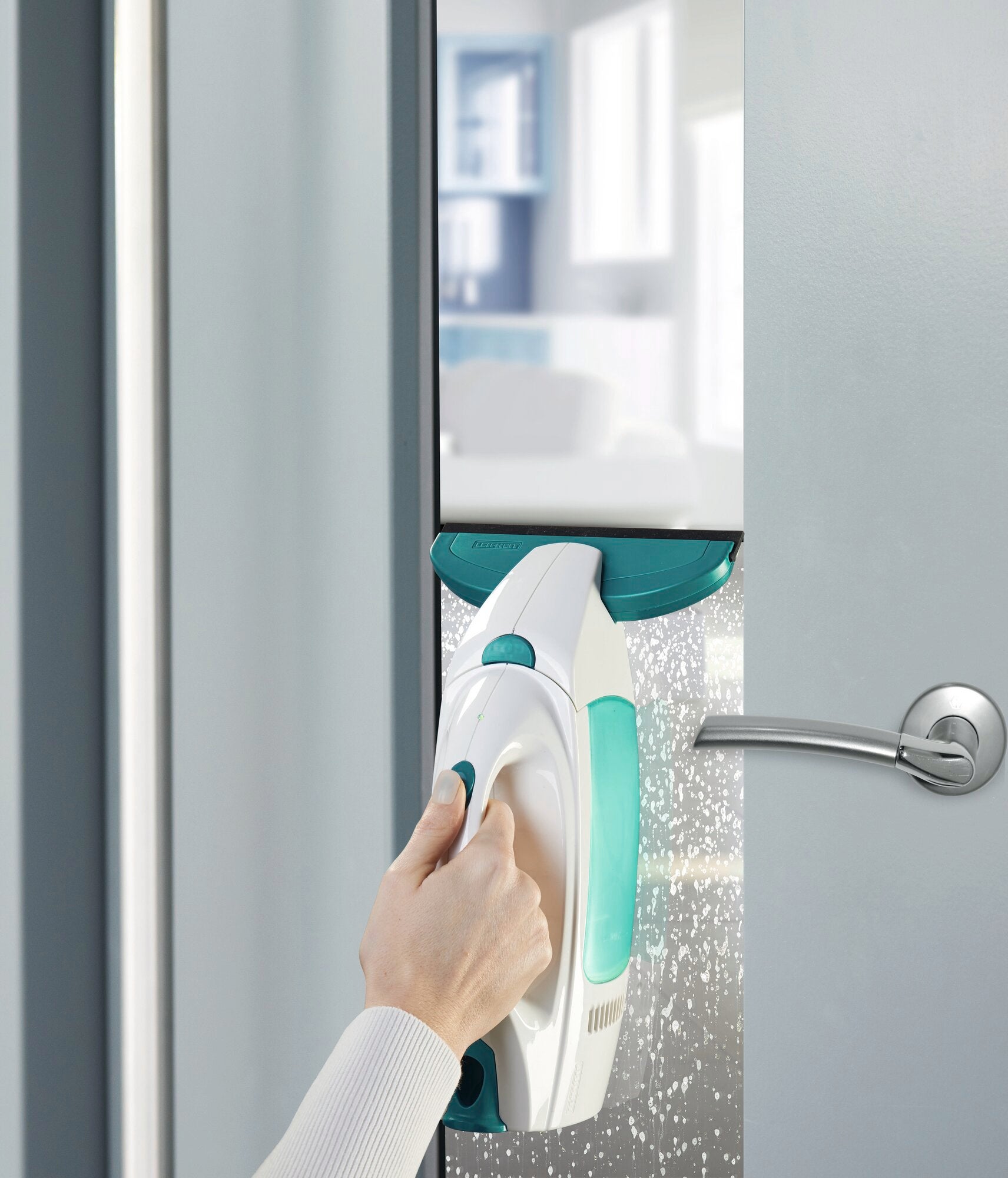 L'aspirapolvere per vetri Dry and Clean con beccuccio piccolo pulisce una porta a vetri. Una mano tiene l'aspirapolvere mentre rimuove efficacemente acqua e sporco. Ideale per finestre senza aloni.