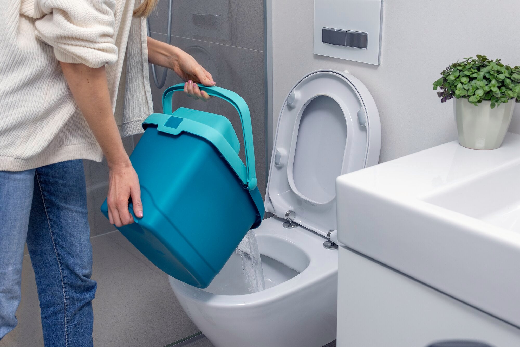 Eine Person gießt Wasser aus einem blauen Eimer in eine Toilette. Der Eimer ist Teil des POWER CLEAN Sets, das für effiziente Reinigungslösungen entwickelt wurde. Im Hintergrund ist ein Badezimmer zu sehen.
