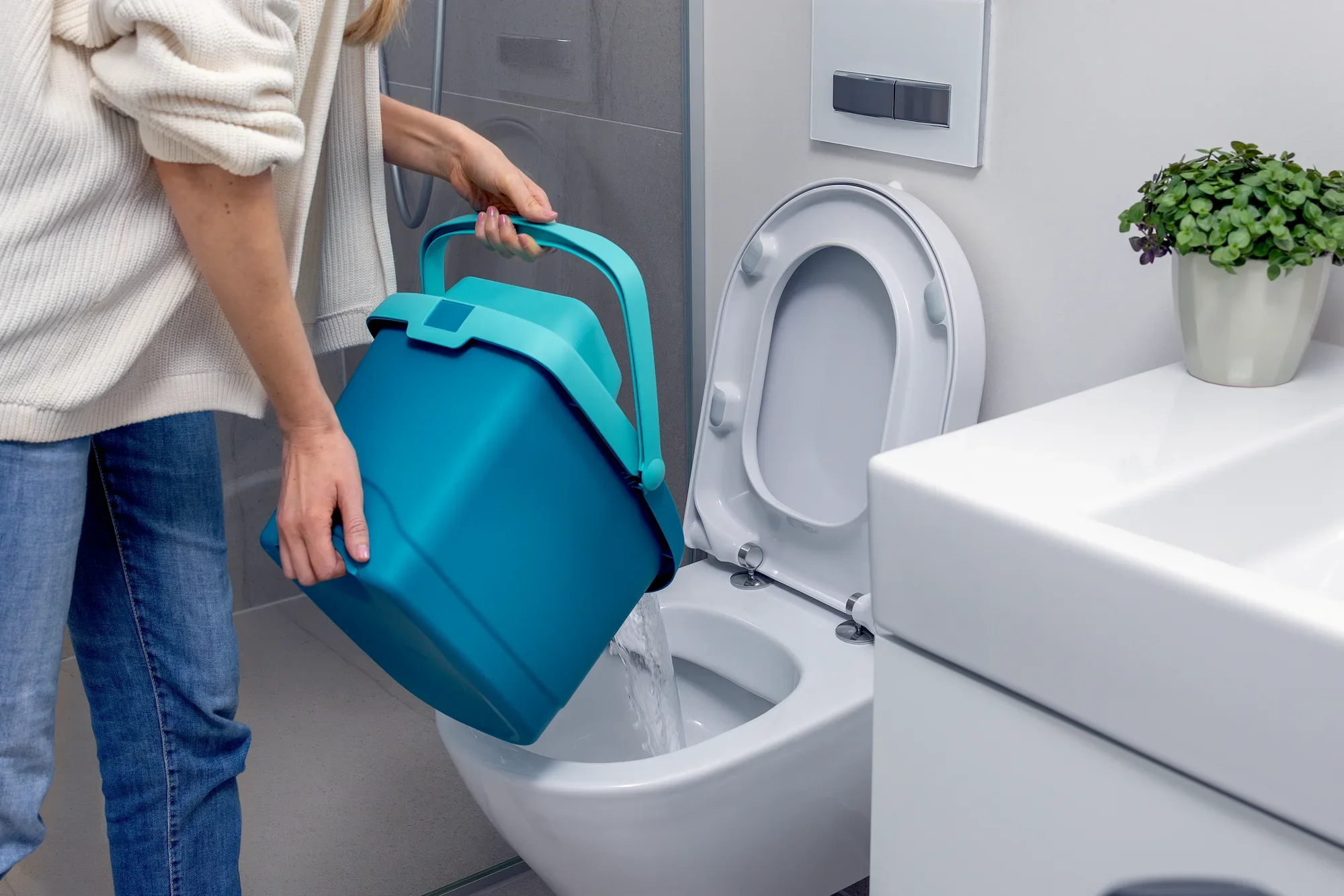 Une personne verse de l'eau d'un seau bleu dans des toilettes. Le seau fait partie du kit POWER CLEAN, conçu pour des solutions de nettoyage efficaces. Une salle de bains est visible à l'arrière-plan.