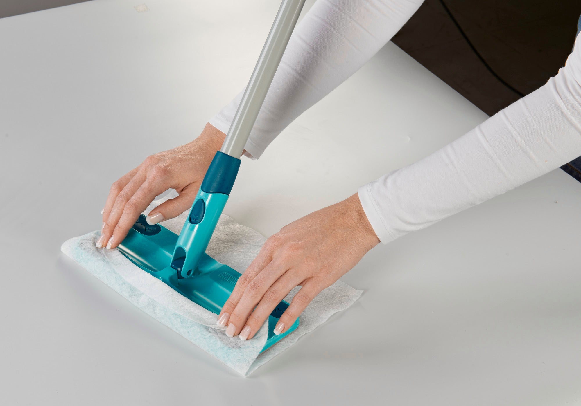 Une personne utilise le kit « Clean and Away » pour nettoyer une surface lisse. La serpillière est dotée d'un manche bleu et d'un chiffon blanc qui garantit un nettoyage efficace.