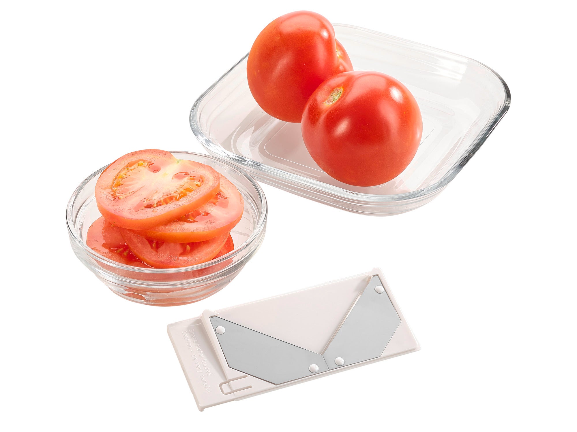 La imagen muestra la rallador multiusos 4+1 en uso. Dos tomates enteros y rodajas de tomate cortadas en cuencos de cristal ilustran la versatilidad del rallador.