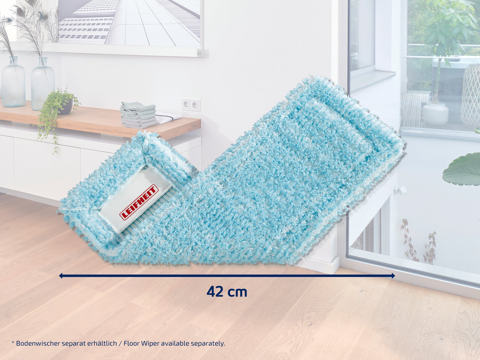 Na drewnianej podłodze w nowoczesnym pomieszczeniu leży turkusowa wycieraczka marki Leifheit. Przystawka ma 42 cm długości i jest idealna do czyszczenia dużych powierzchni.